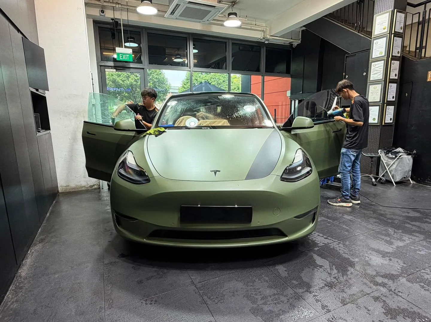 A pale green Tesla roadster with technicians working on both sides.