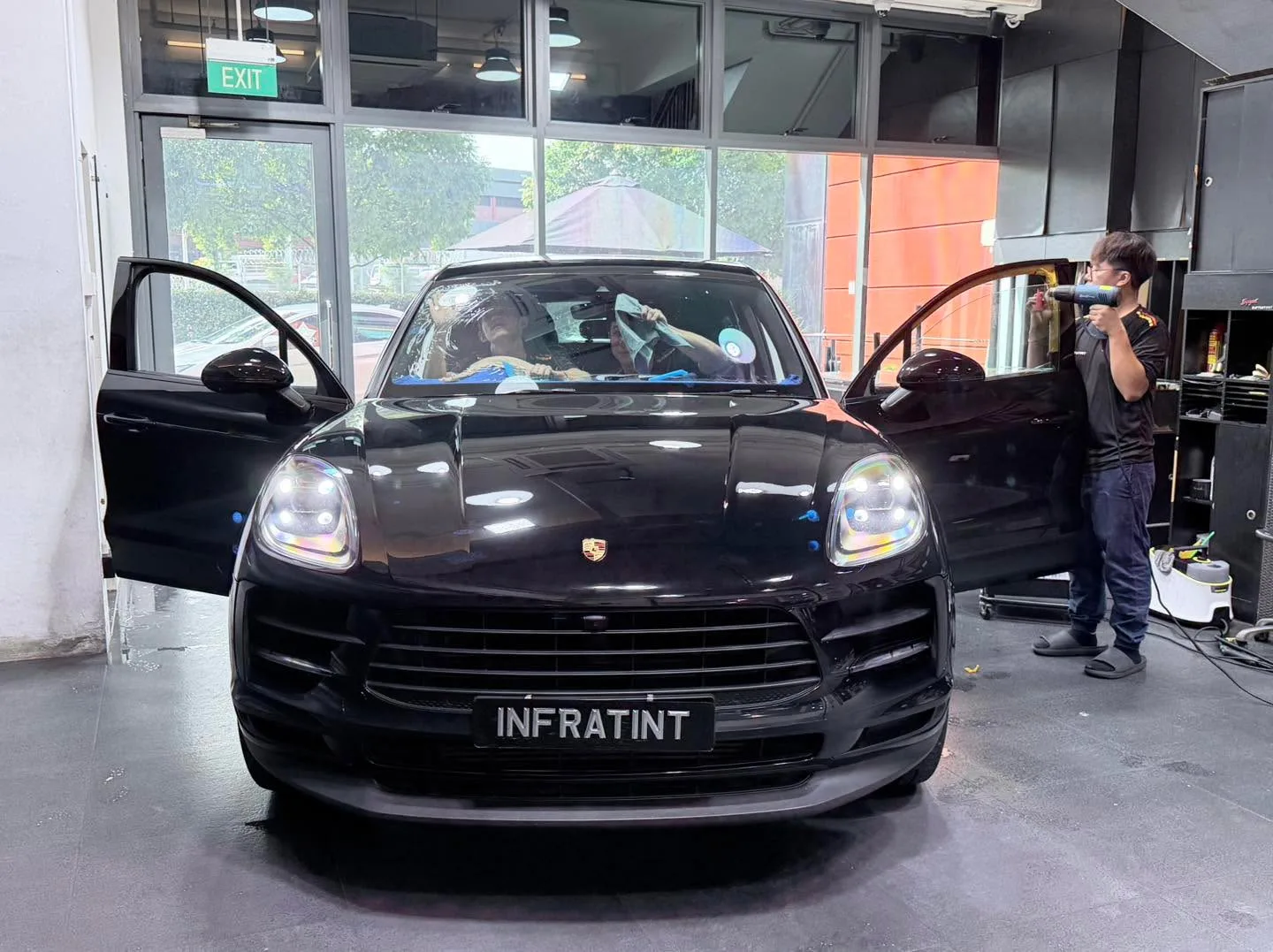 Black Porsche Macan with doors open, technician applying tint film to windows.