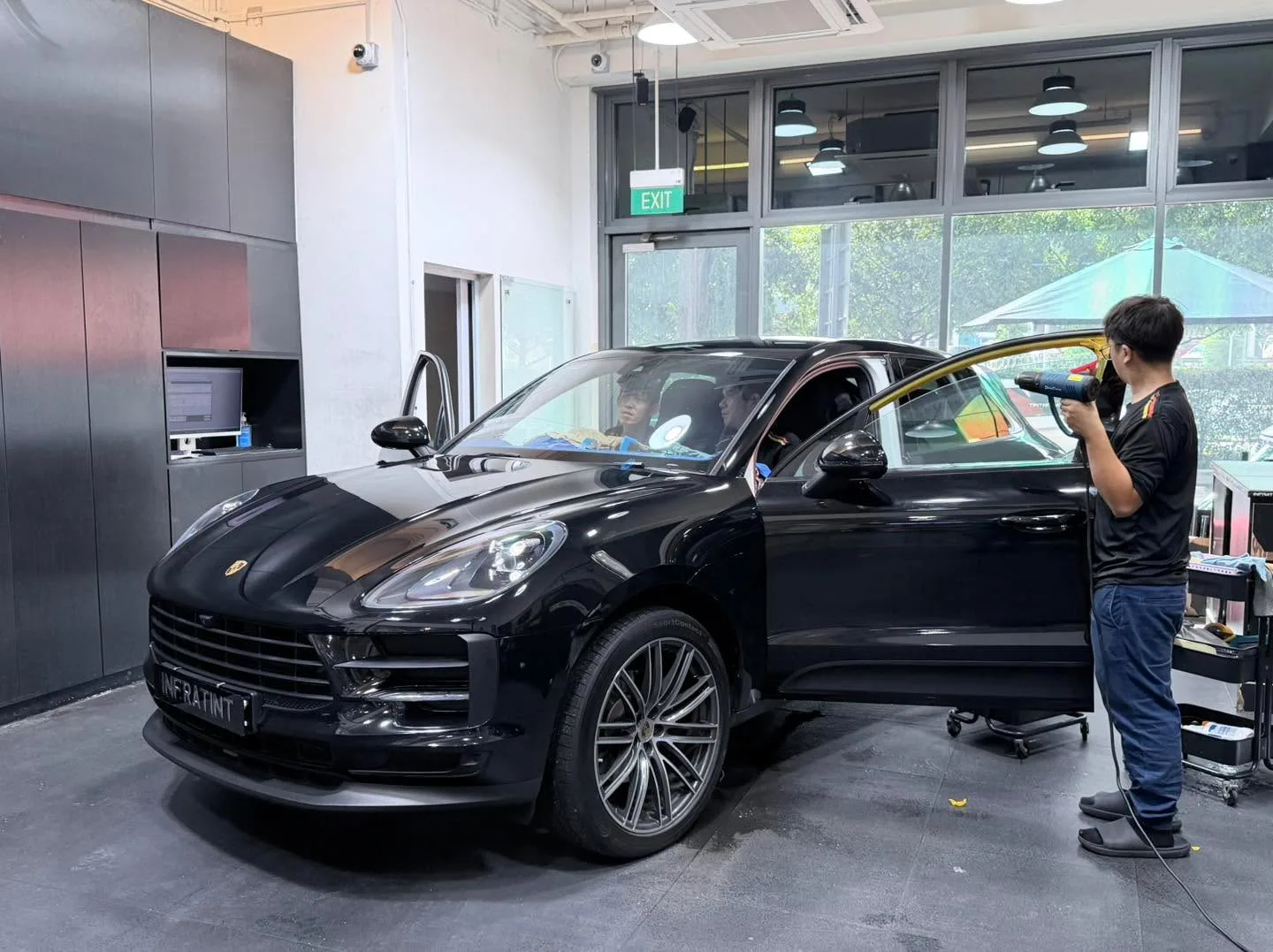 Grey Tesla electric sedan with doors open inside the workshop, technician applying tint.