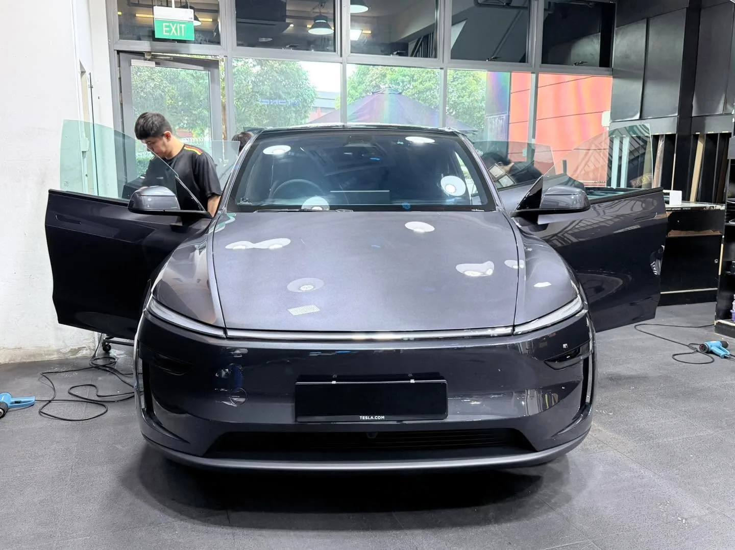 Grey electric SUV with gull-wing doors open, technician working on the windows.