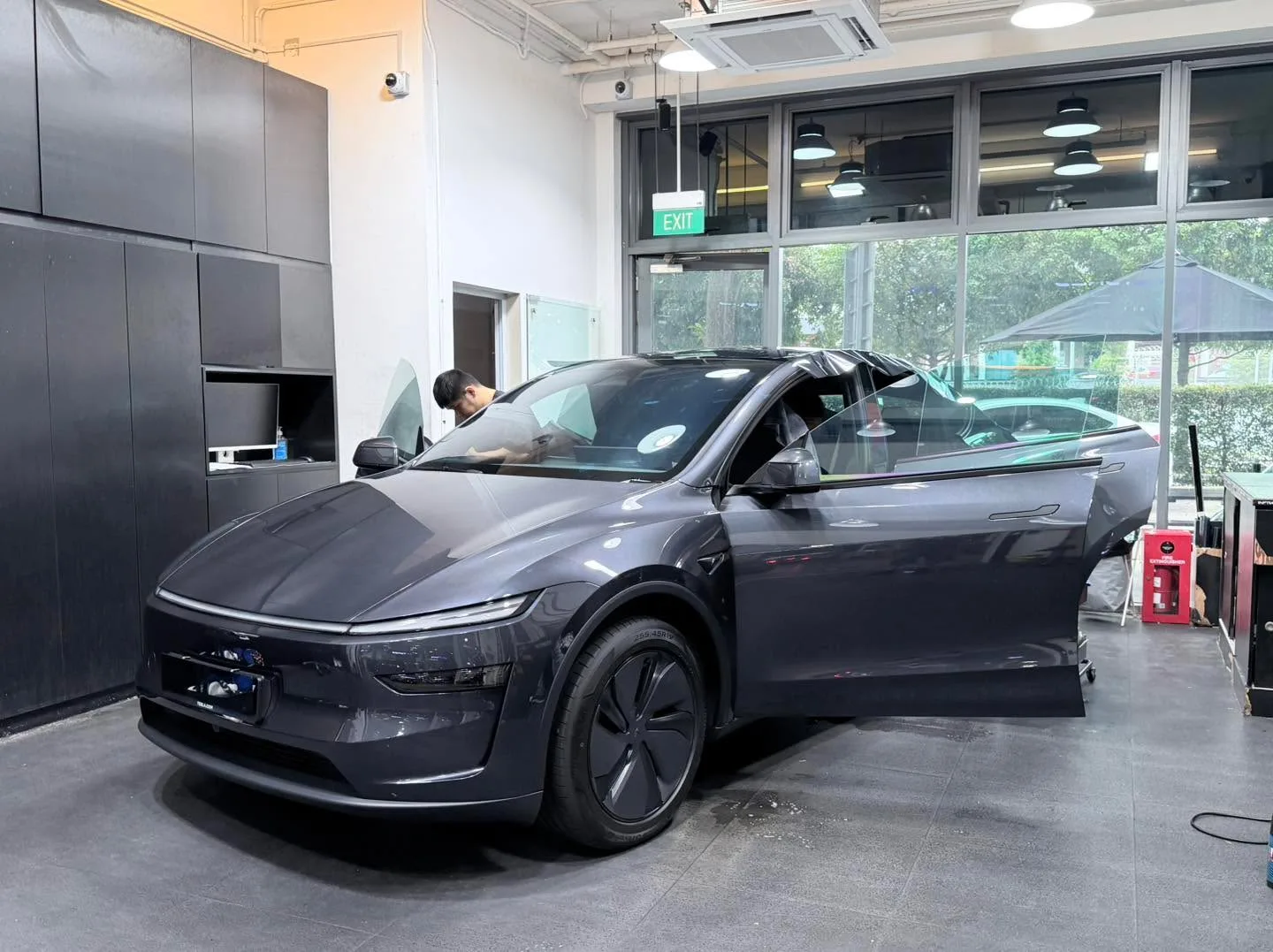 Silver-grey compact electric hatchback with doors open, technician tinting side windows.