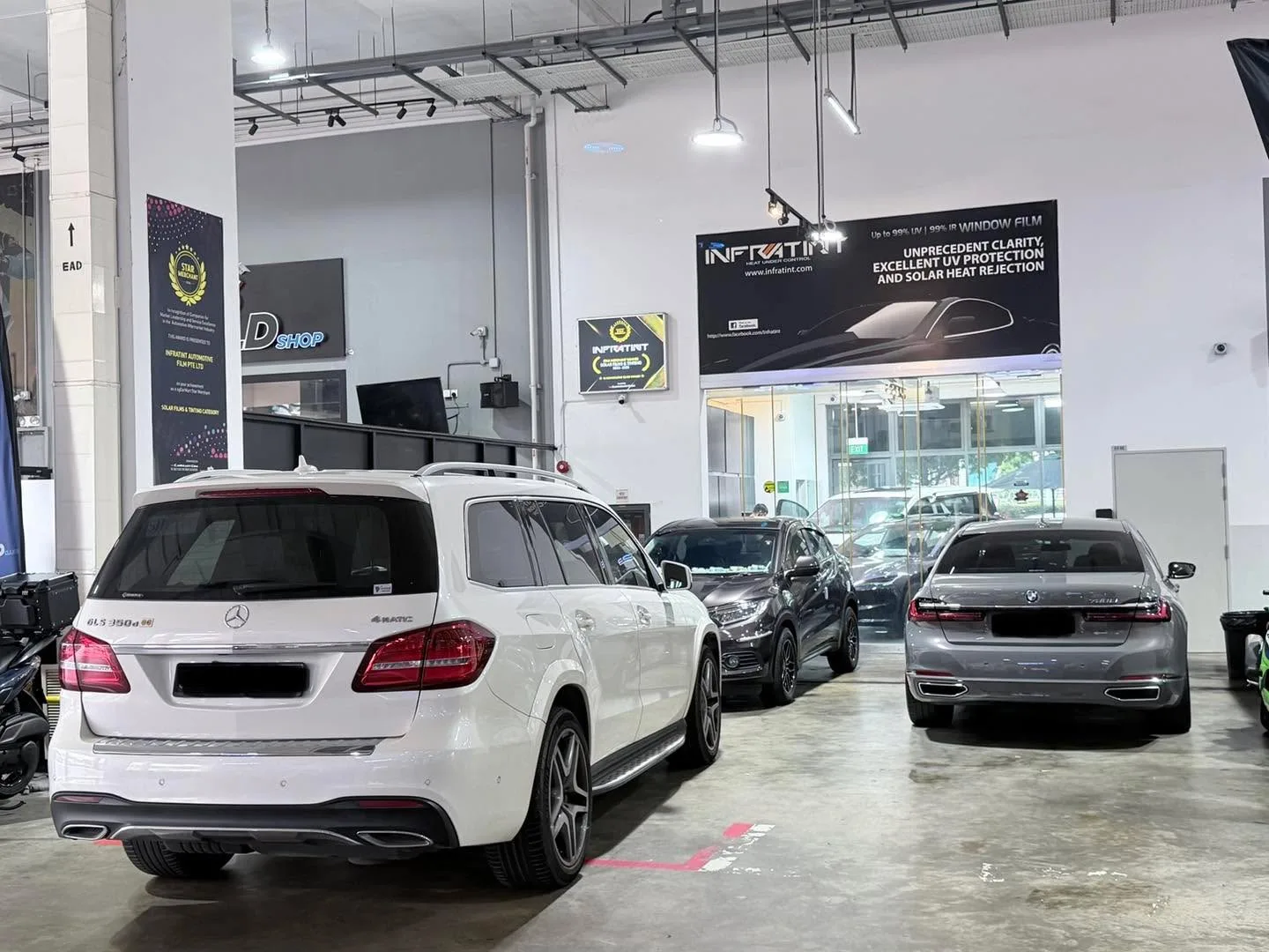 A white Mercedes-Benz compact SUV, a black car, and a silver sedan parked indoors at Infratint workshop.
