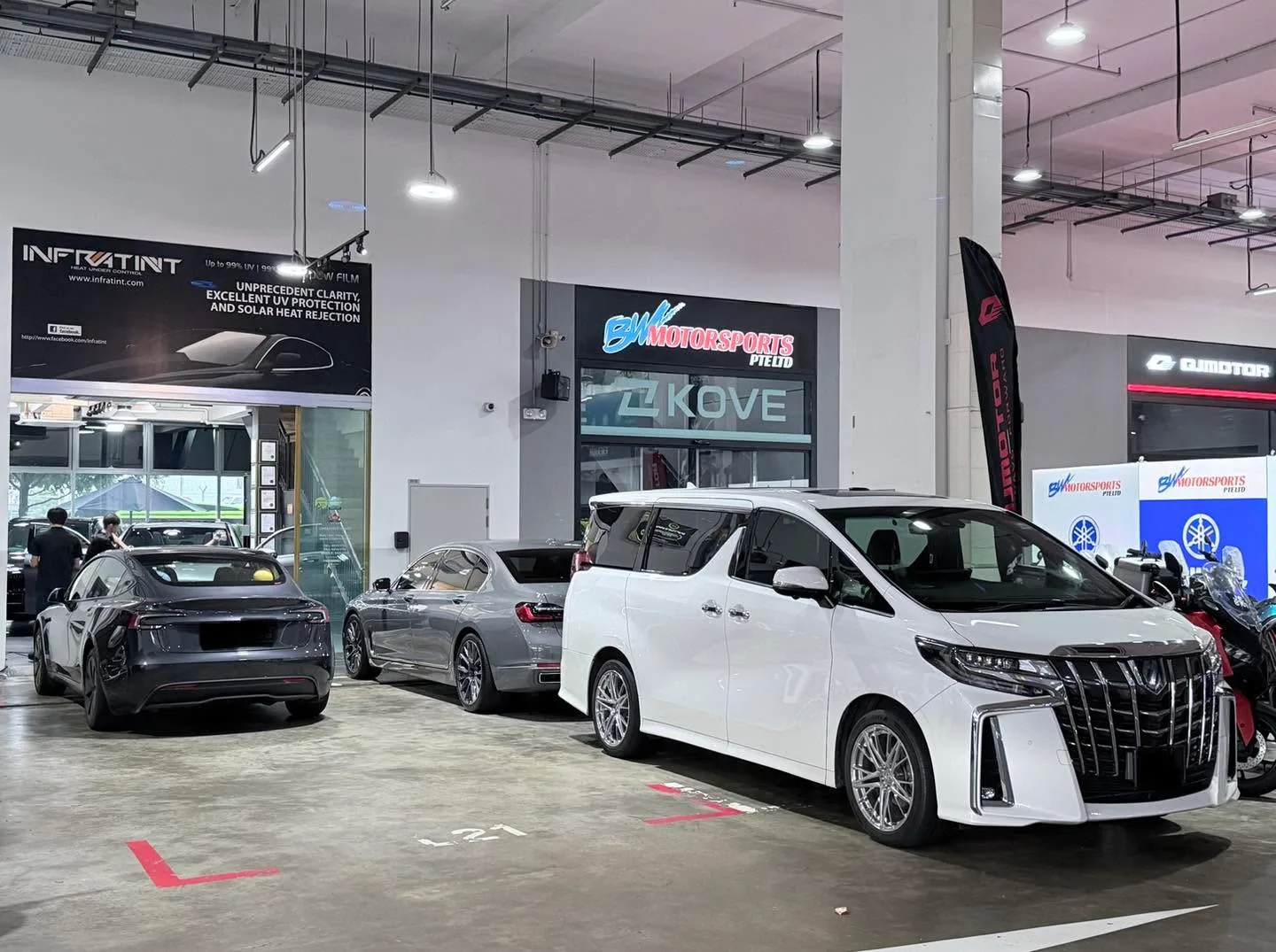 A white Toyota Alphard minivan and a black sports car parked in the workshop, with staff visible.