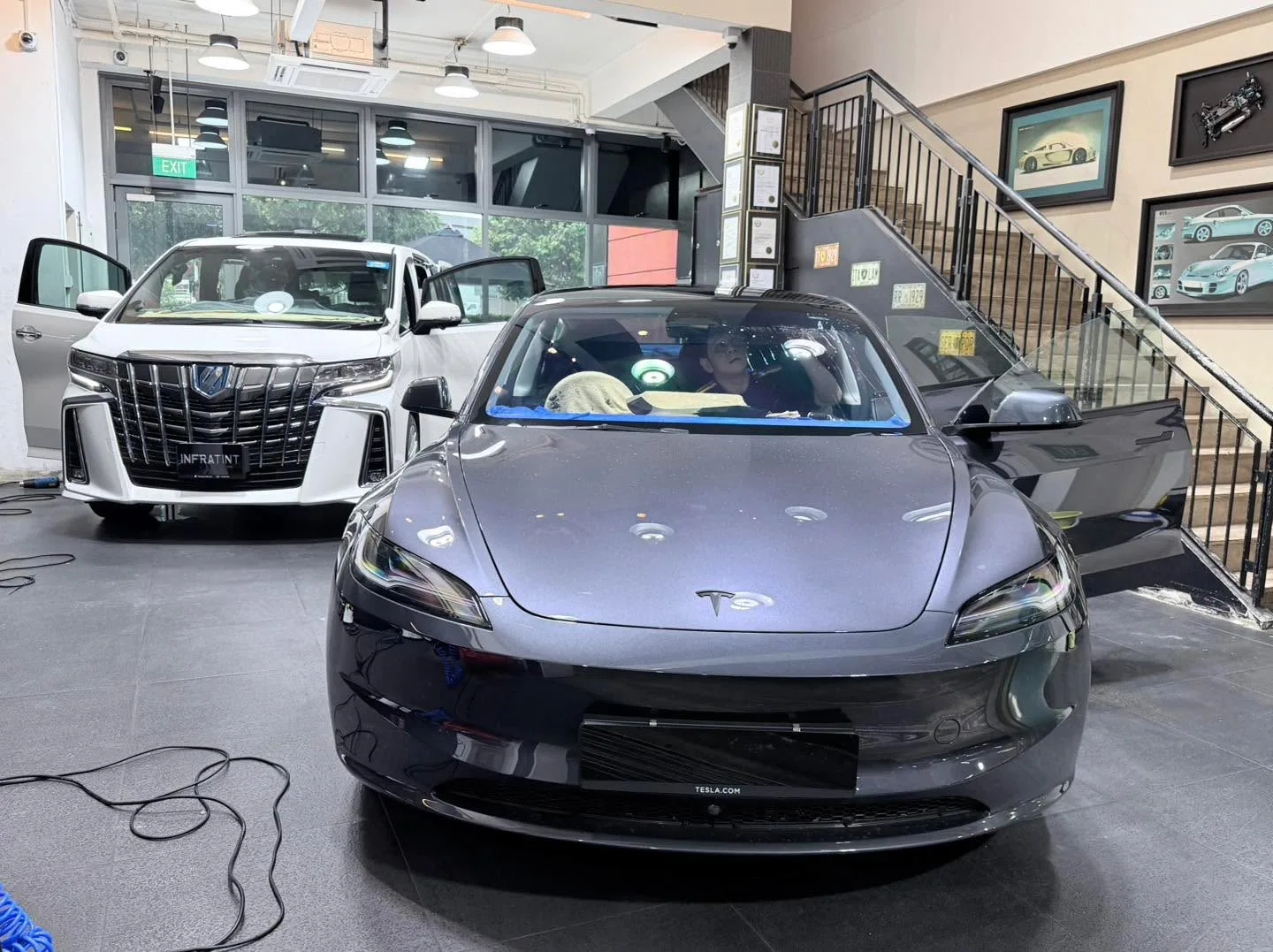 A dark grey Tesla Model 3 sedan viewed from the front in the workshop bay.