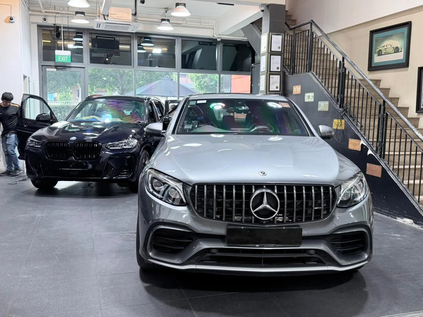 A silver Mercedes-Benz GLC 63S SUV viewed from the front, with a dark BMW SUV behind it.