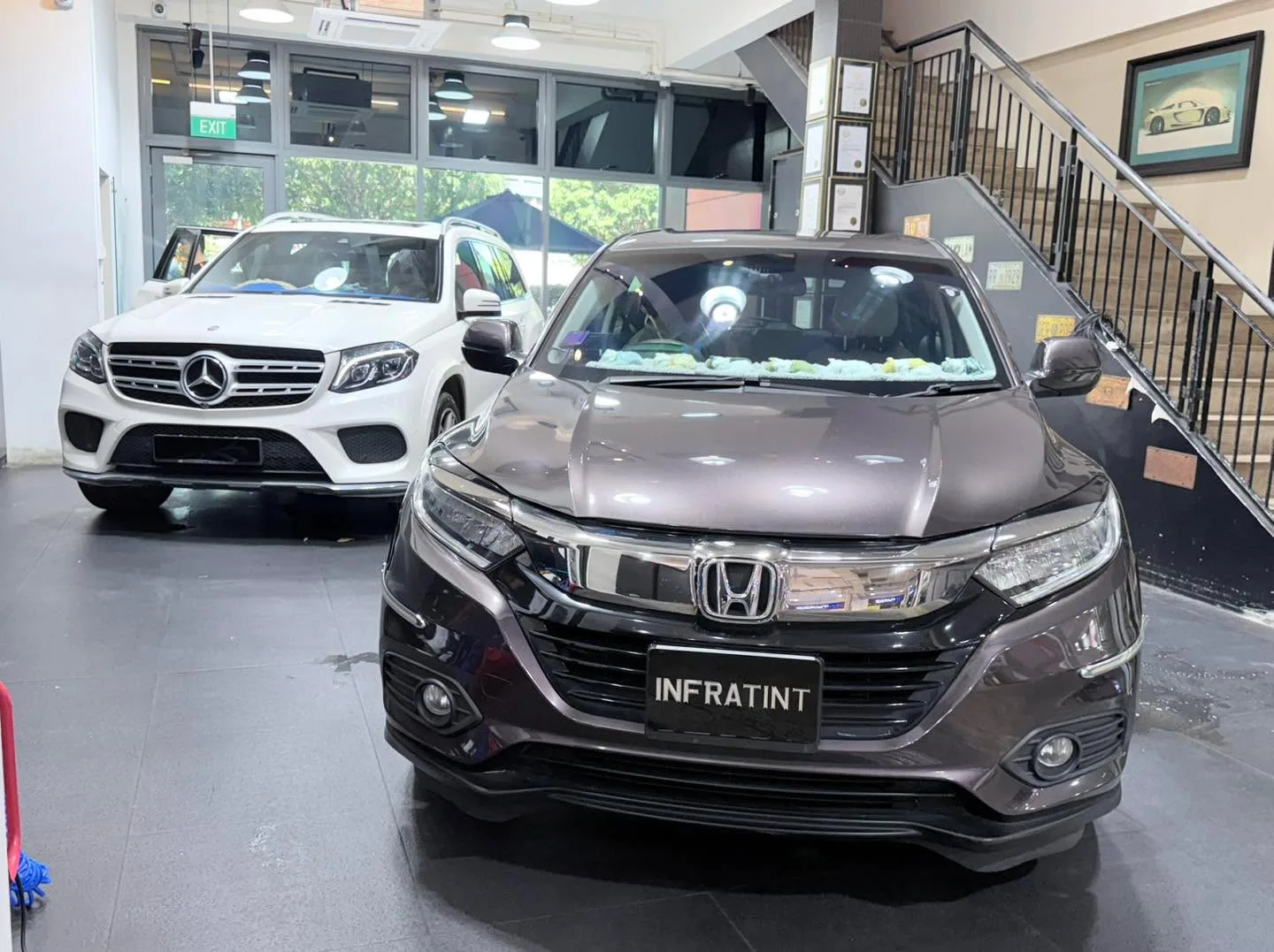 A white Mercedes-Benz GLS SUV parked next to a black Honda Vezel, indoors at workshop.