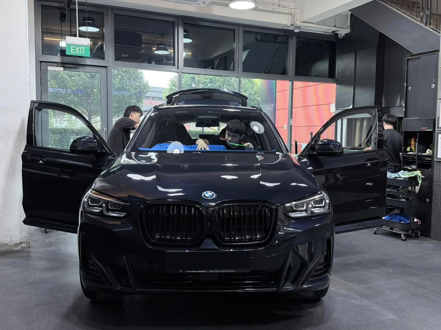 A black BMW iX3 electric SUV with doors open, viewed from the front in workshop.