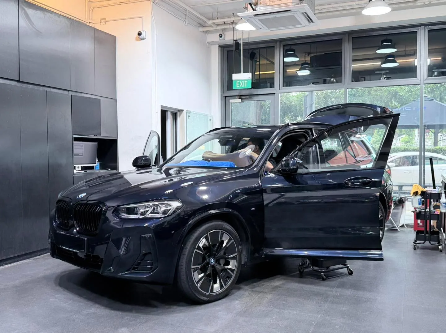 A black BMW iX3 SUV with boot open, parked in the workshop with staff beside it.