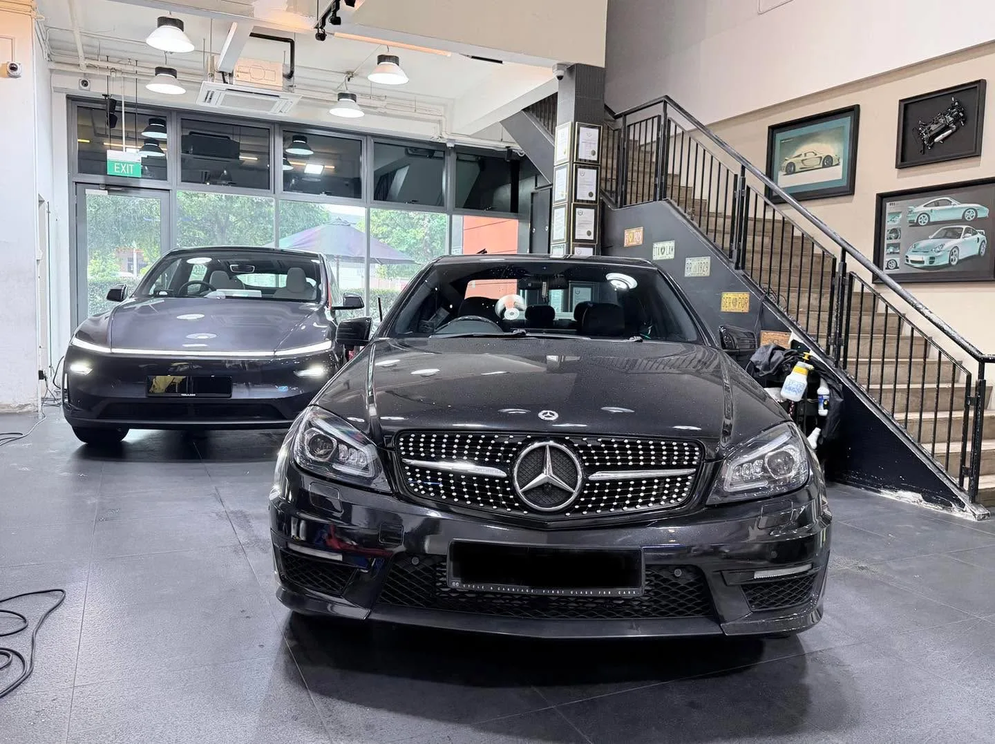 Front view of a black Mercedes-Benz C-Class with distinctive grille, silver sedan to its right, and technicians working on the black car.