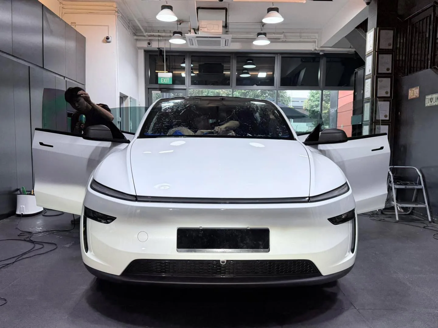 White Tesla sedan with doors open, technician applying window film with yellow protective covering on windows.