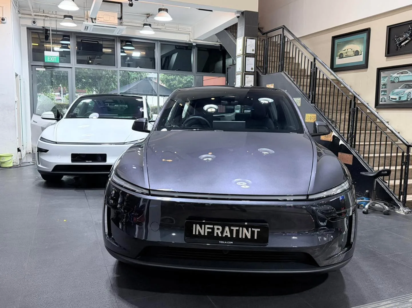 A dark grey Tesla Model Y with tinted windows viewed from the front at the workshop showroom.