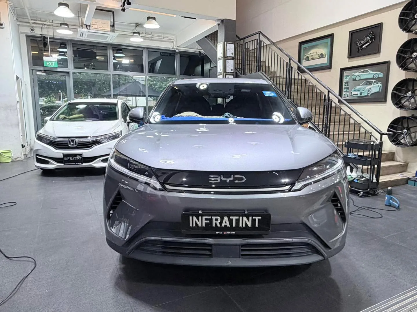 A dark grey BYD Atto 3 crossover and a white Tesla Model Y crossover parked side by side indoors.