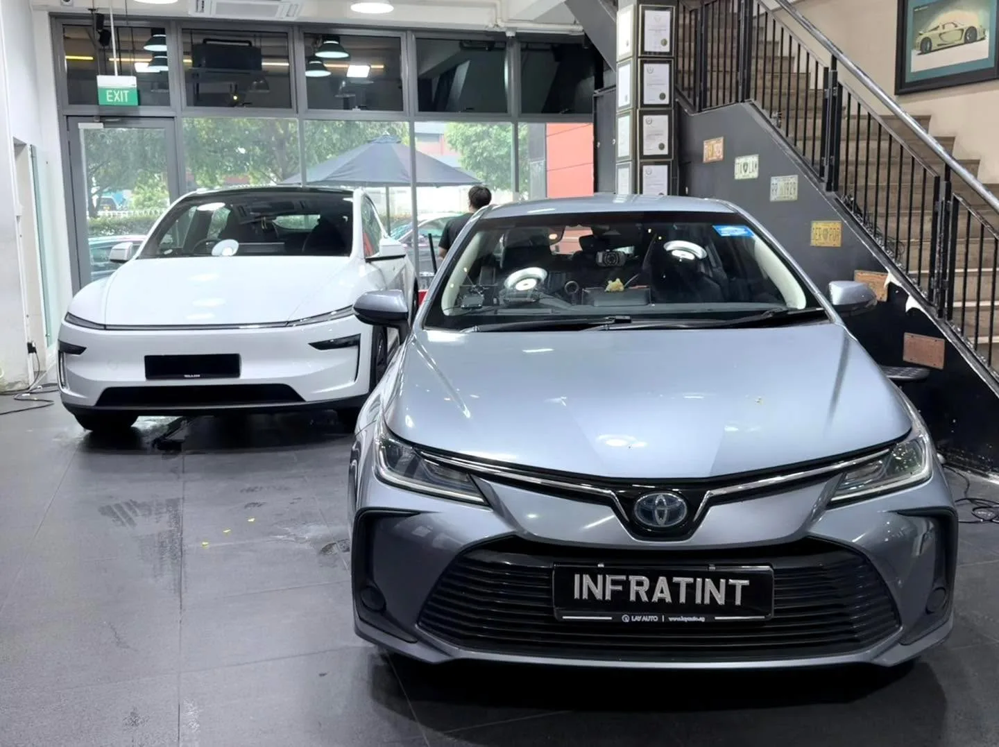 A silver Toyota Corolla saloon and a white Tesla Model Y crossover viewed from the front indoors.
