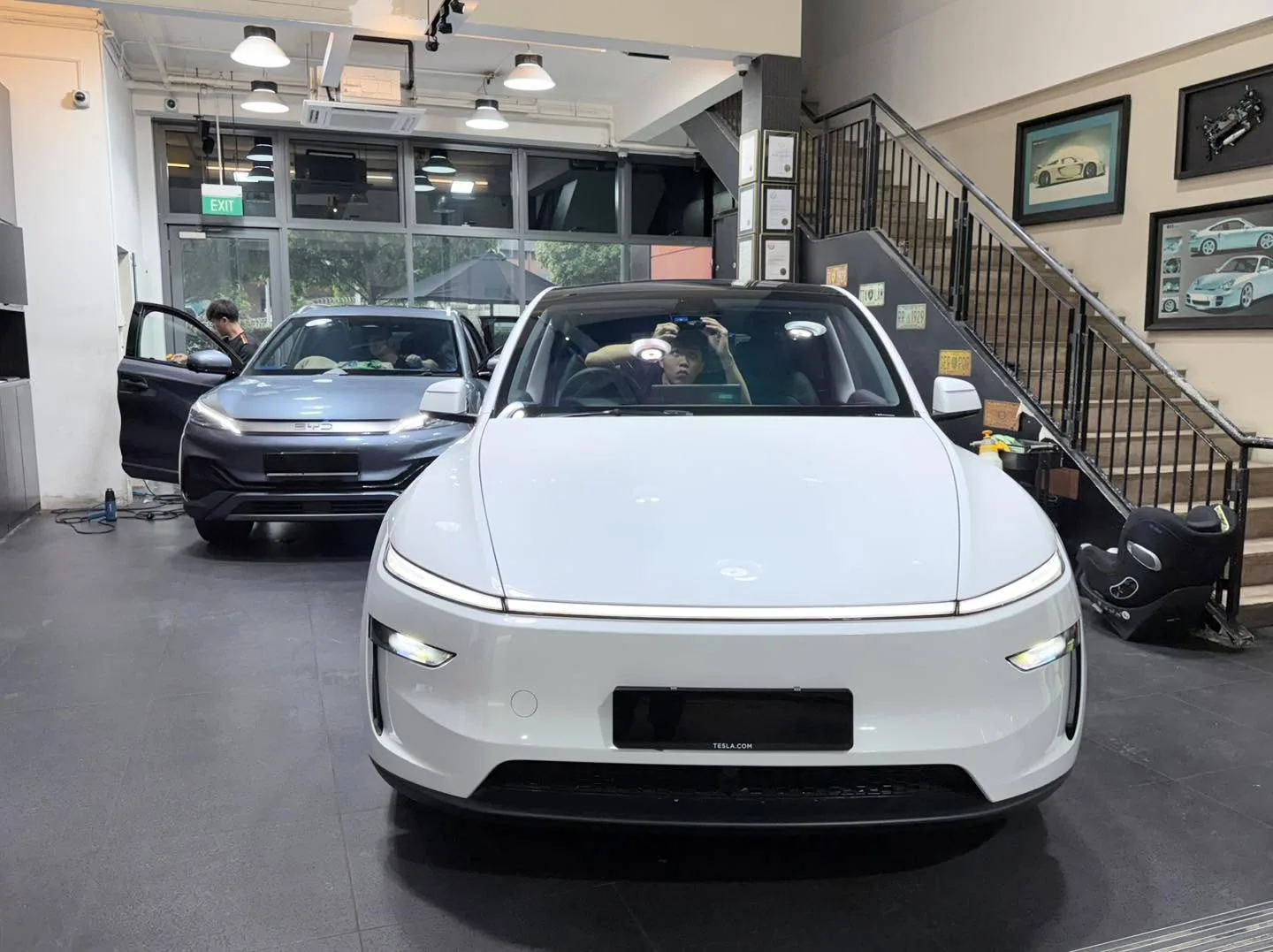A dark blue Volkswagen Scirocco coupe and a black Tesla Model Y crossover parked indoors.