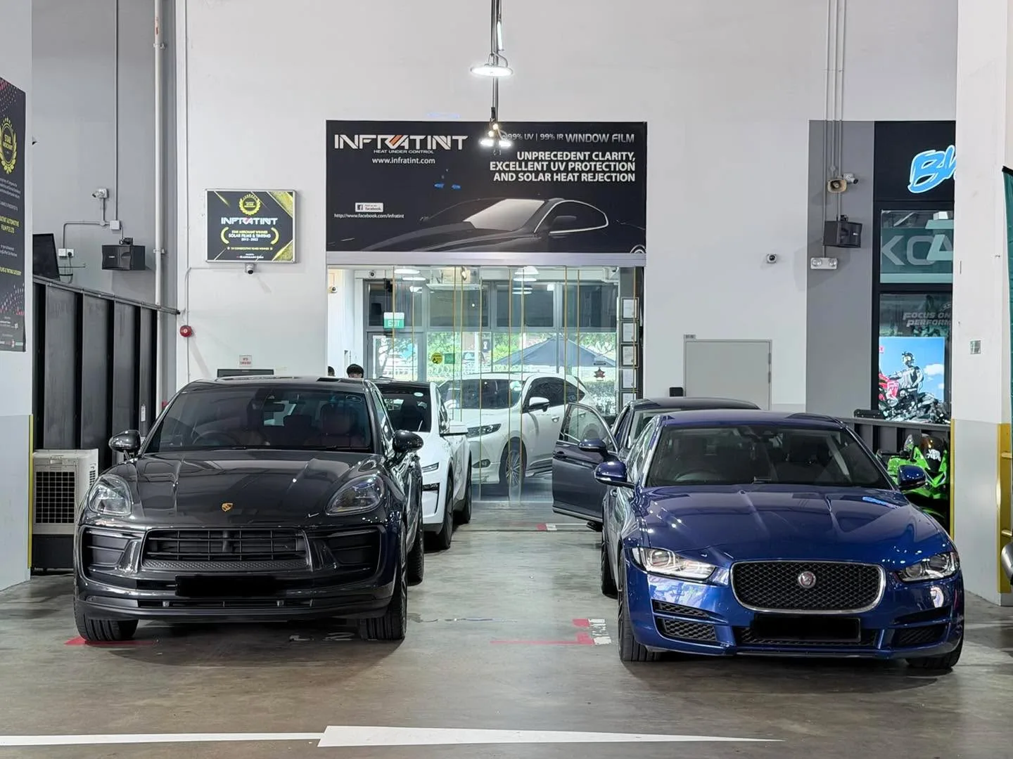 A black Porsche Macan and blue Jaguar XE parked side by side in the workshop.