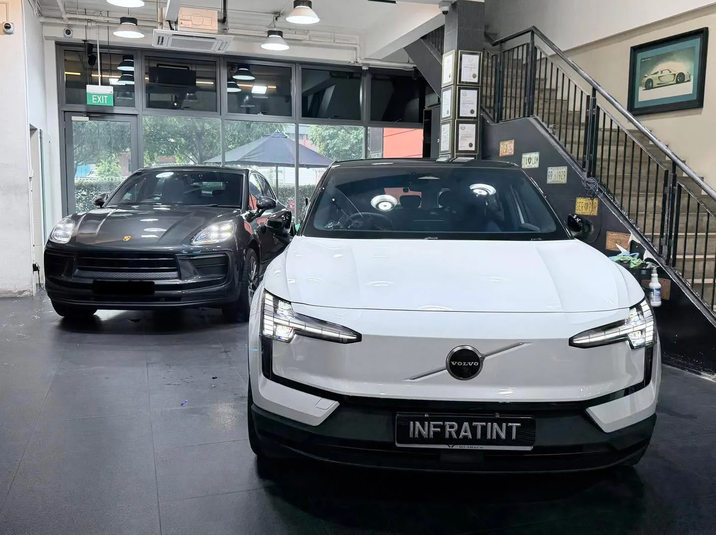 A white Volvo EX30 and black Porsche Macan parked indoors under bright lighting.