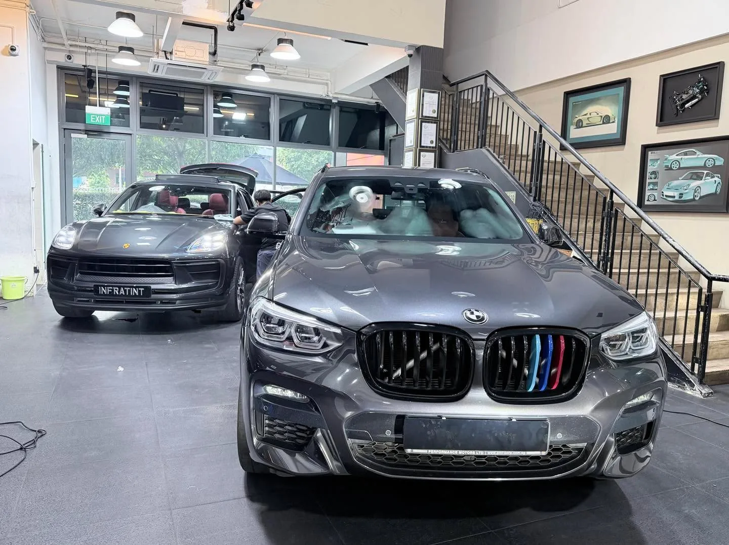 A black Porsche Macan with the door open, parked next to a white Volvo EX30.