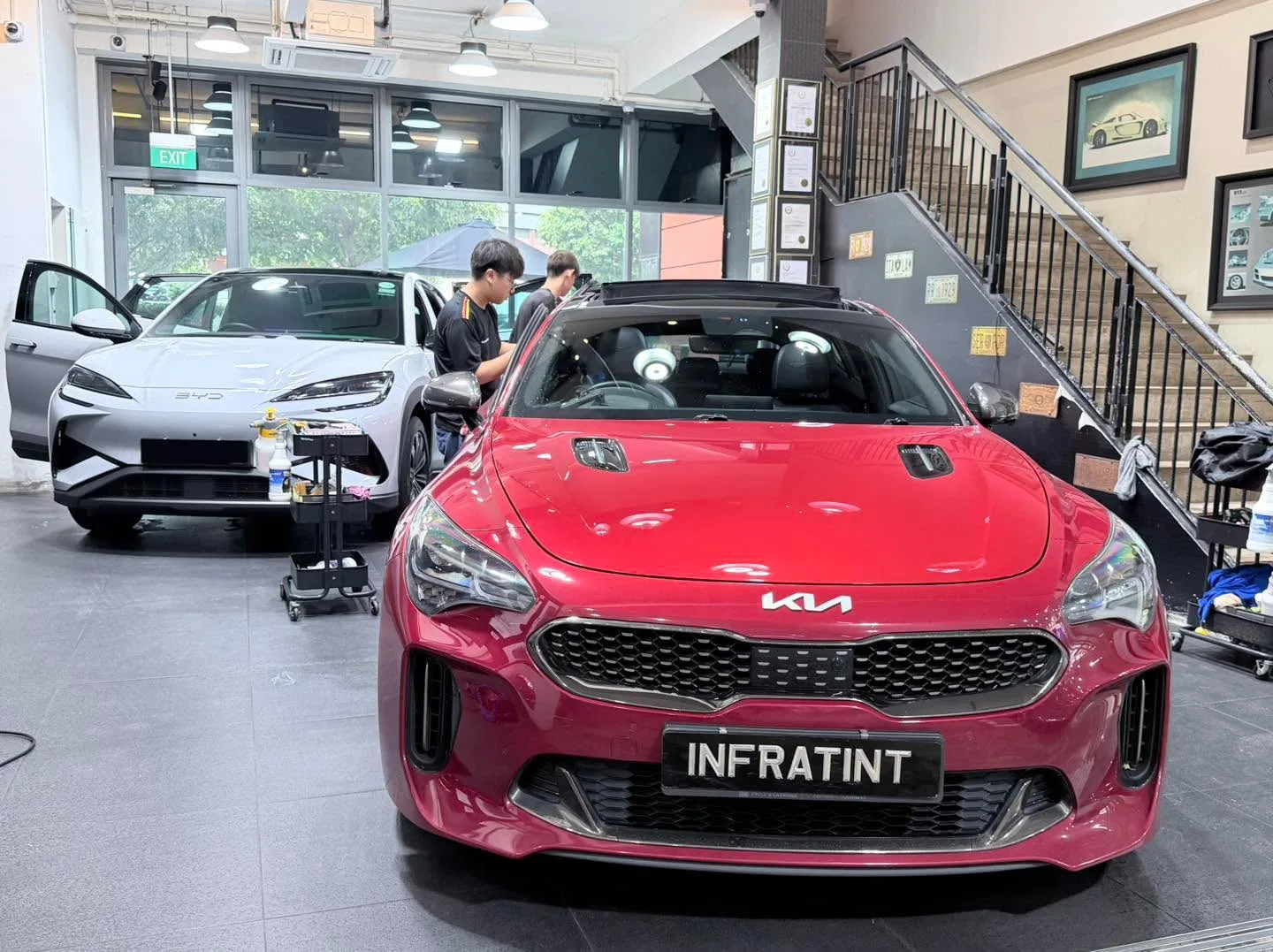 A red Kia compact car with staff applying window tint in the workshop.