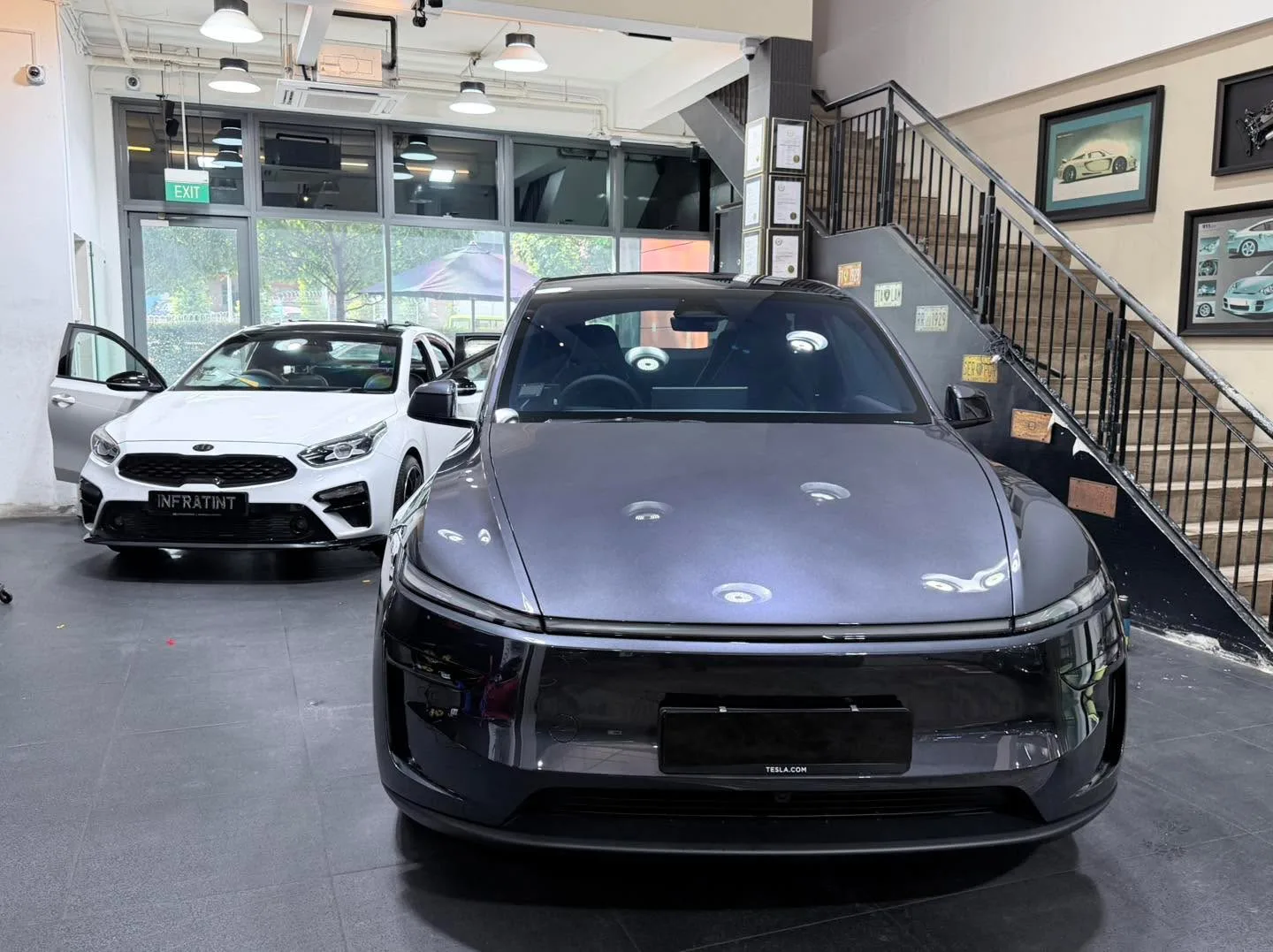 A dark-coloured Tesla sedan and a white Kia with red accents inside the showroom.