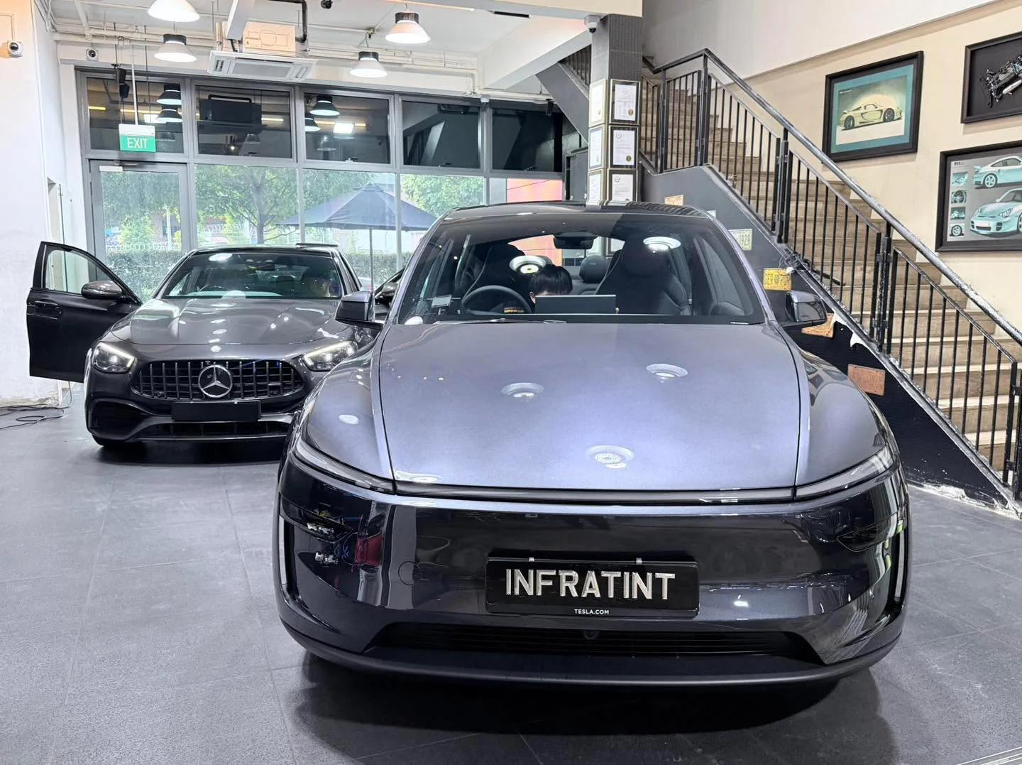 A dark Tesla Model Y sedan and a dark Mercedes-Benz coupe inside the showroom.