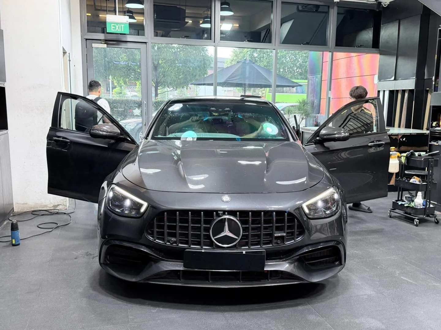 A dark Mercedes-Benz sedan with both doors open and technicians working on the windows.