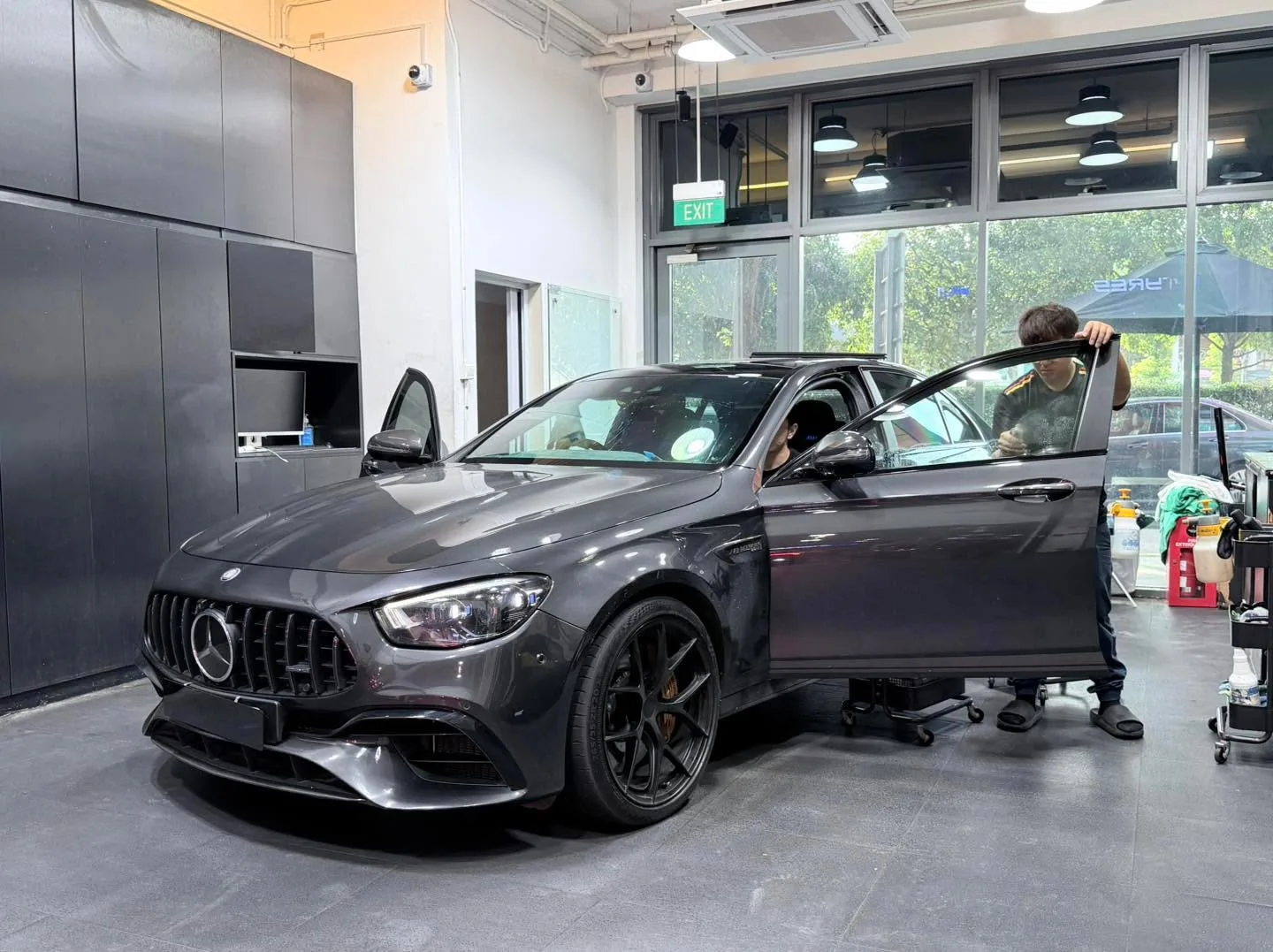 A dark Mercedes-Benz coupe with an open door and a technician applying tint to the windows.