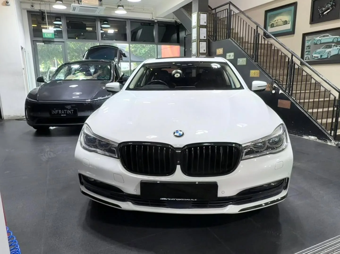 A white BMW X3 from the front, parked indoors with a dark Tesla sedan visible behind it.
