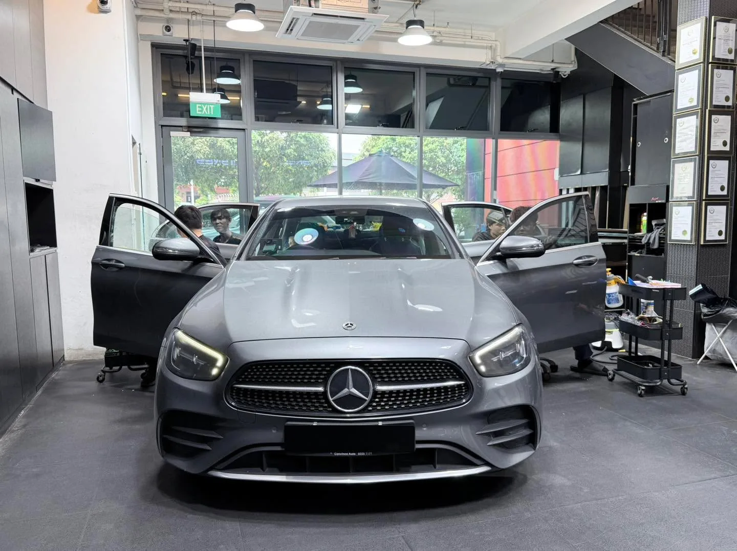 A grey Mercedes-Benz E-Class with doors open, parked in the workshop during tinting work.