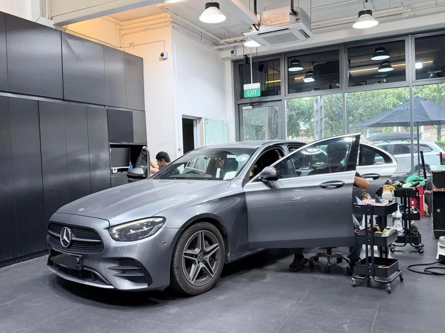 A grey Mercedes-Benz E-Class coupe positioned in the workshop with doors open.