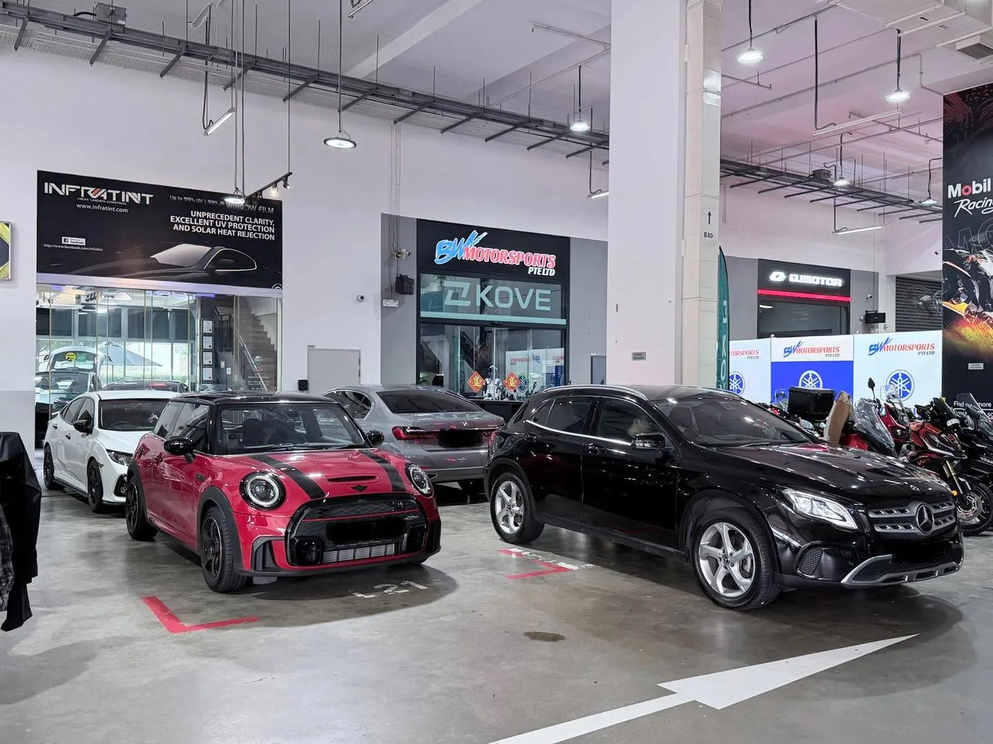 A red Mini hatchback, a grey sedan, and a black Mercedes-Benz SUV parked indoors at the workshop.