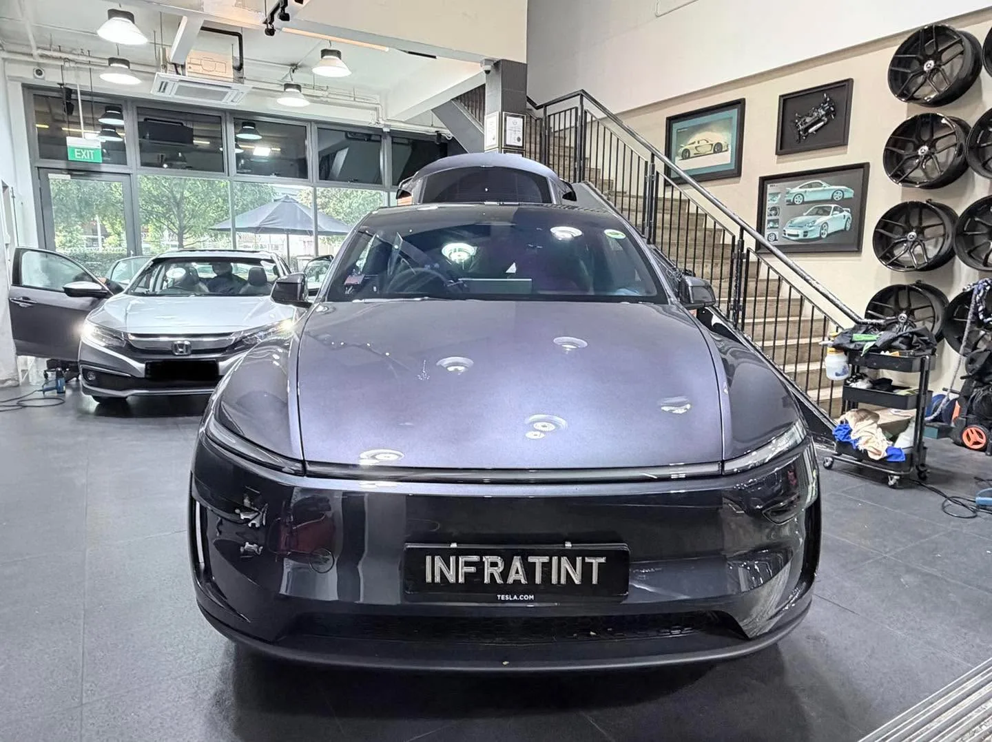 A grey Tesla sedan with the Infratint licence plate, parked indoors with shop windows behind.