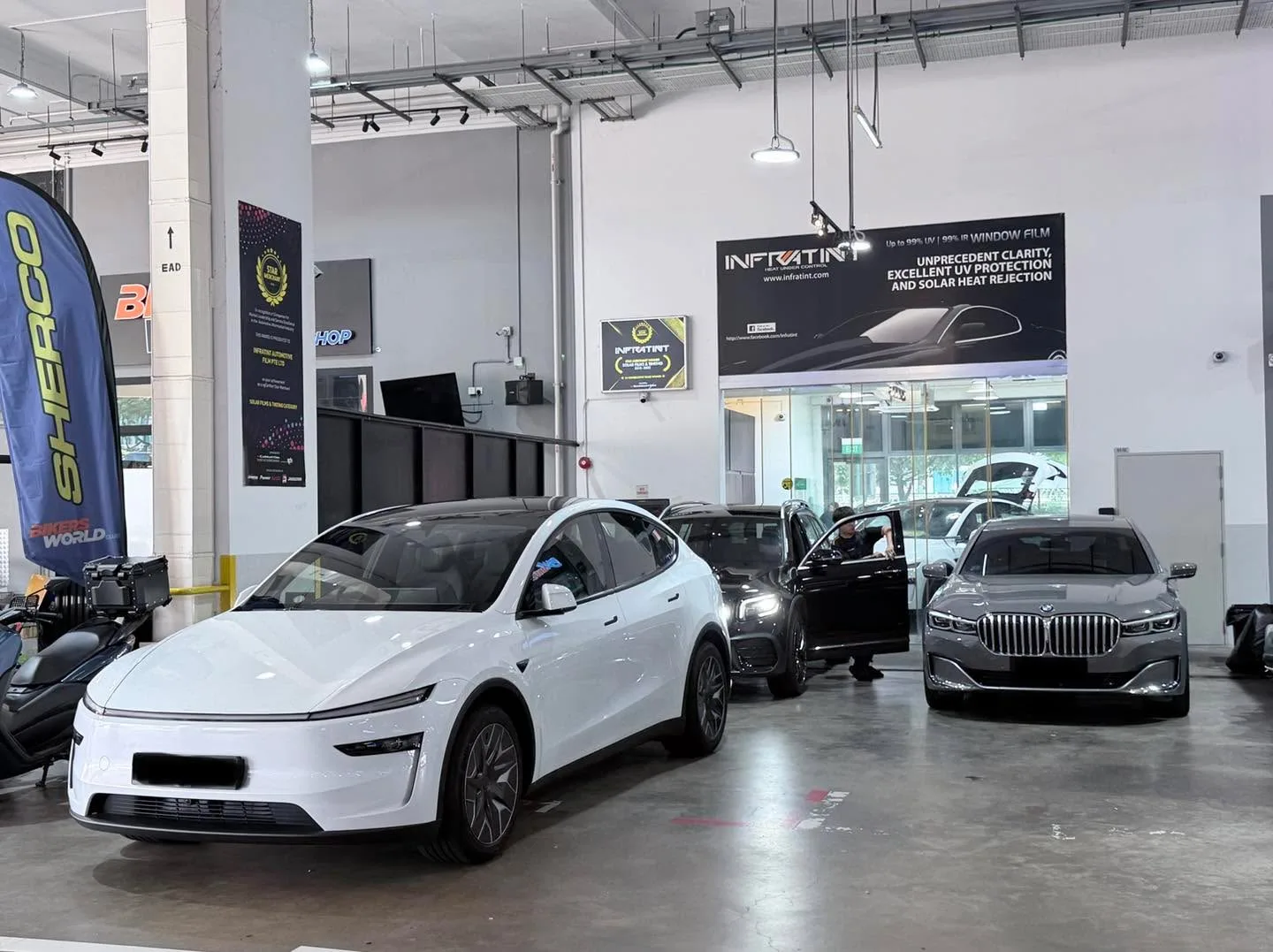 A white Tesla saloon and a grey premium saloon inside the workshop bay, with a black SUV in the background.