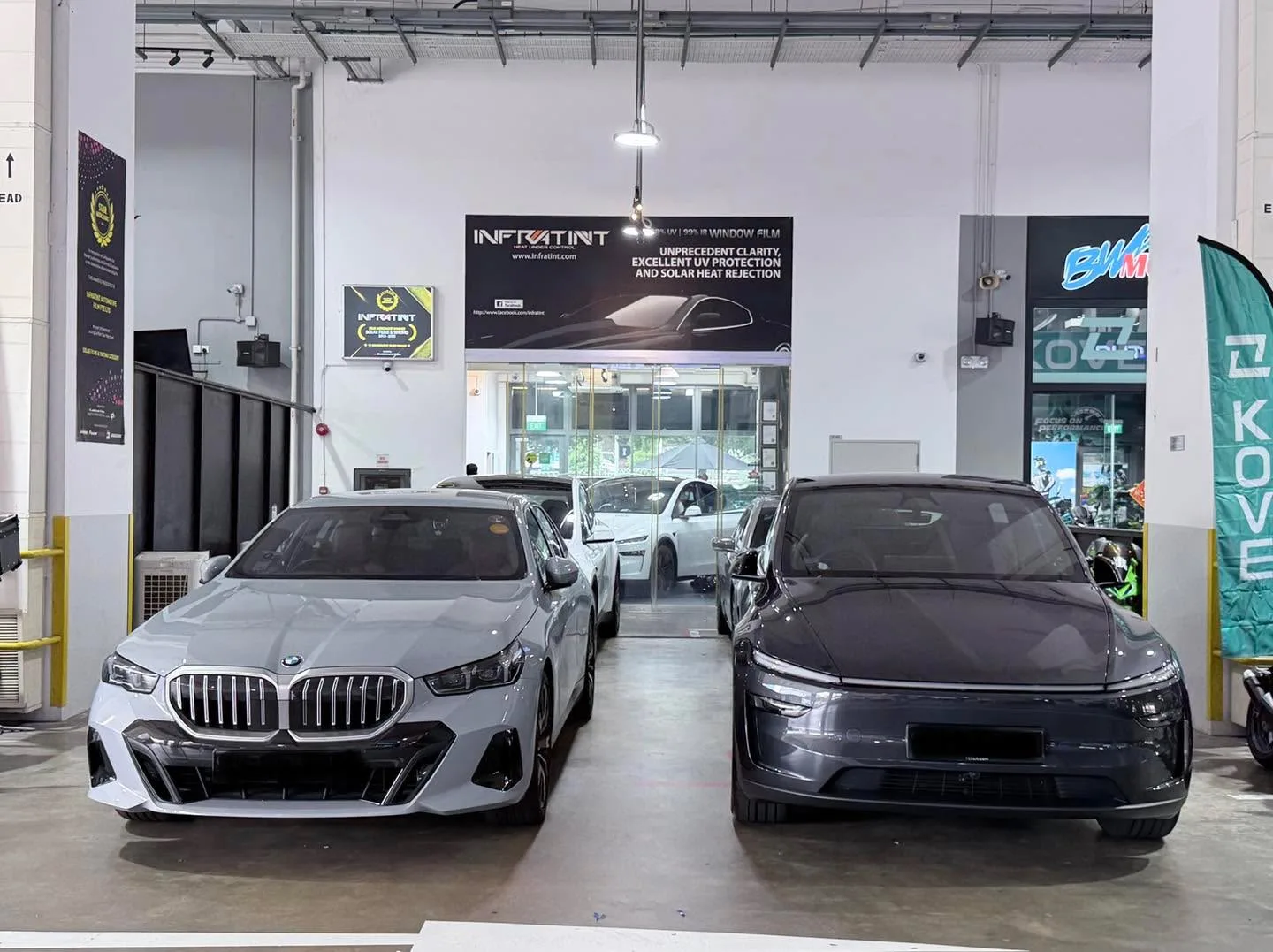 A white BMW saloon and a black electric saloon parked in the workshop, alongside other vehicles.