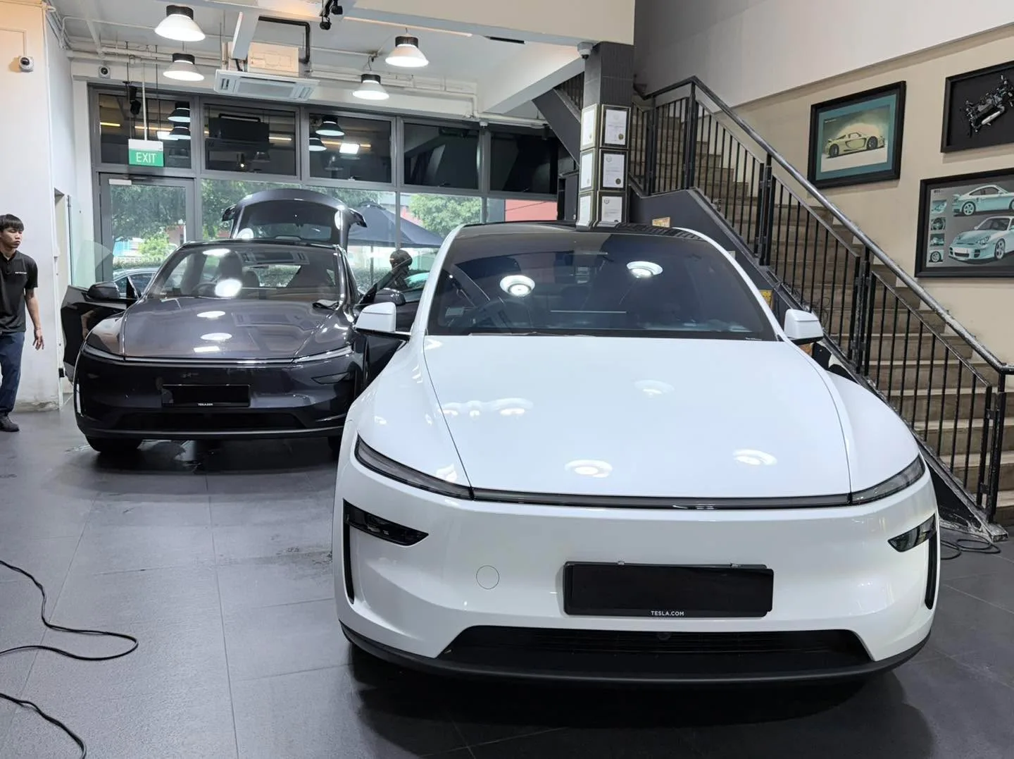 A white Tesla saloon in the foreground with a black saloon beside it in the workshop space.