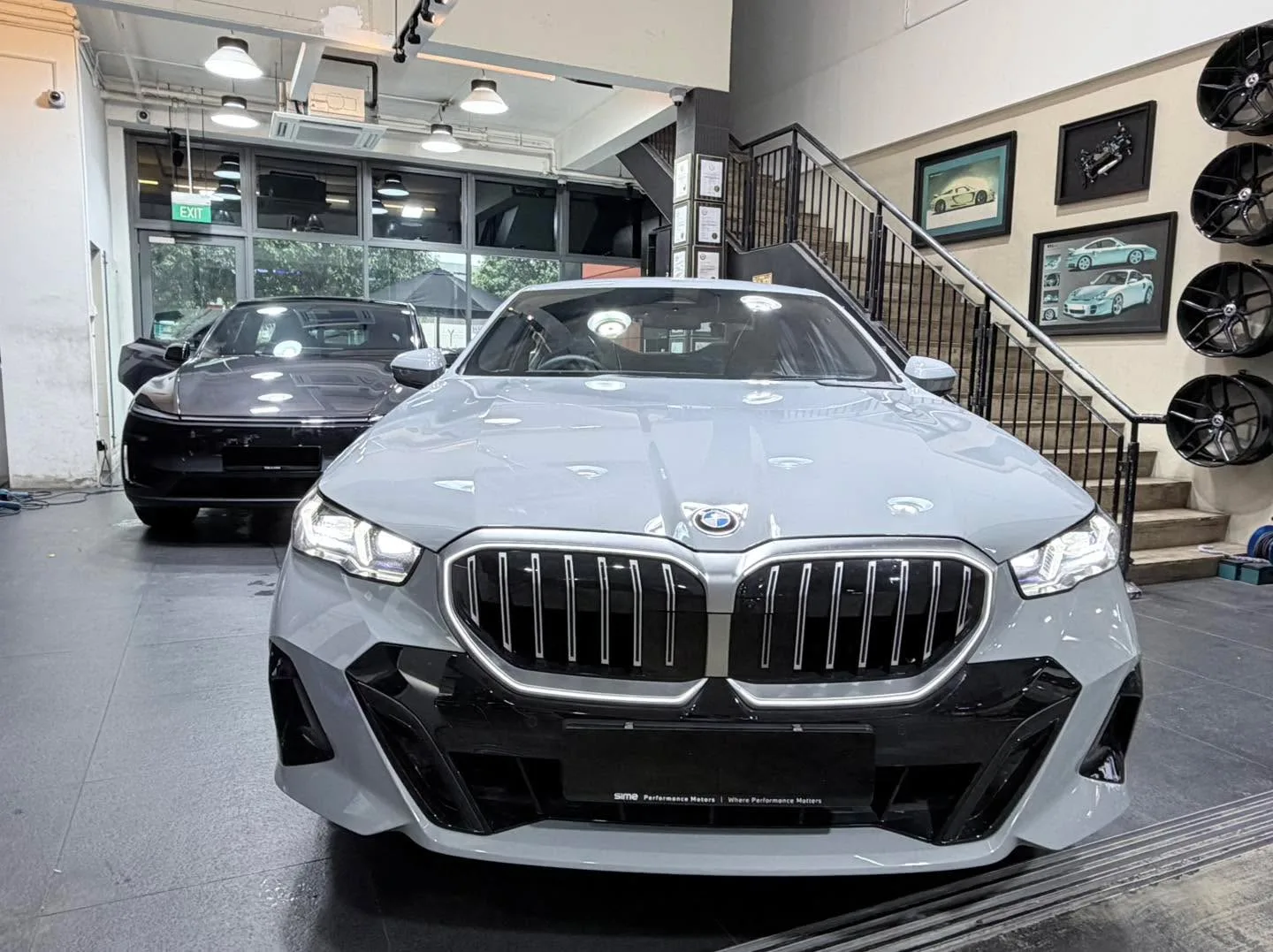A grey BMW saloon with distinctive grille parked in the workshop beside another vehicle.