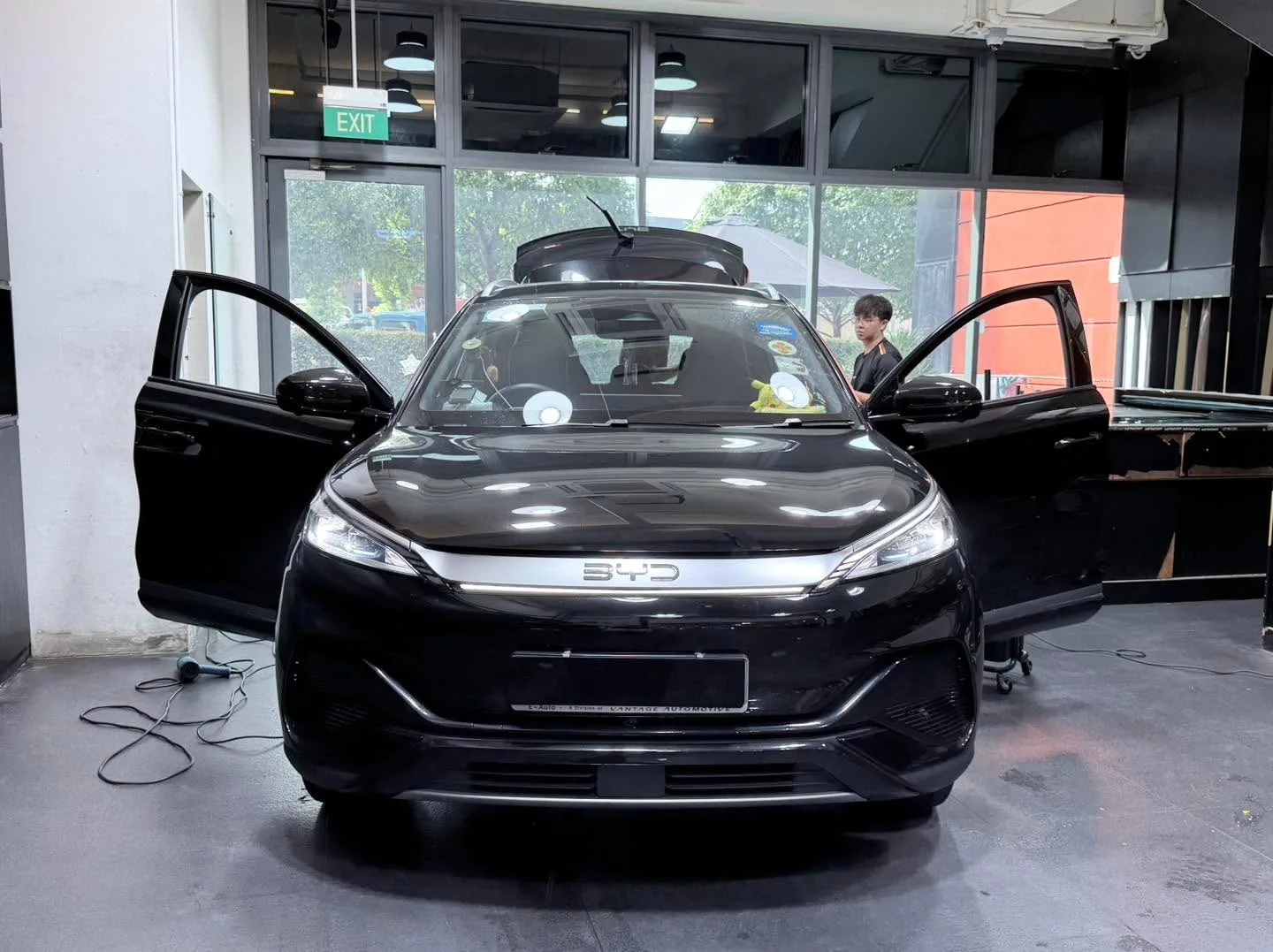 A black BYD crossover with both doors open inside the workshop under bright lights.