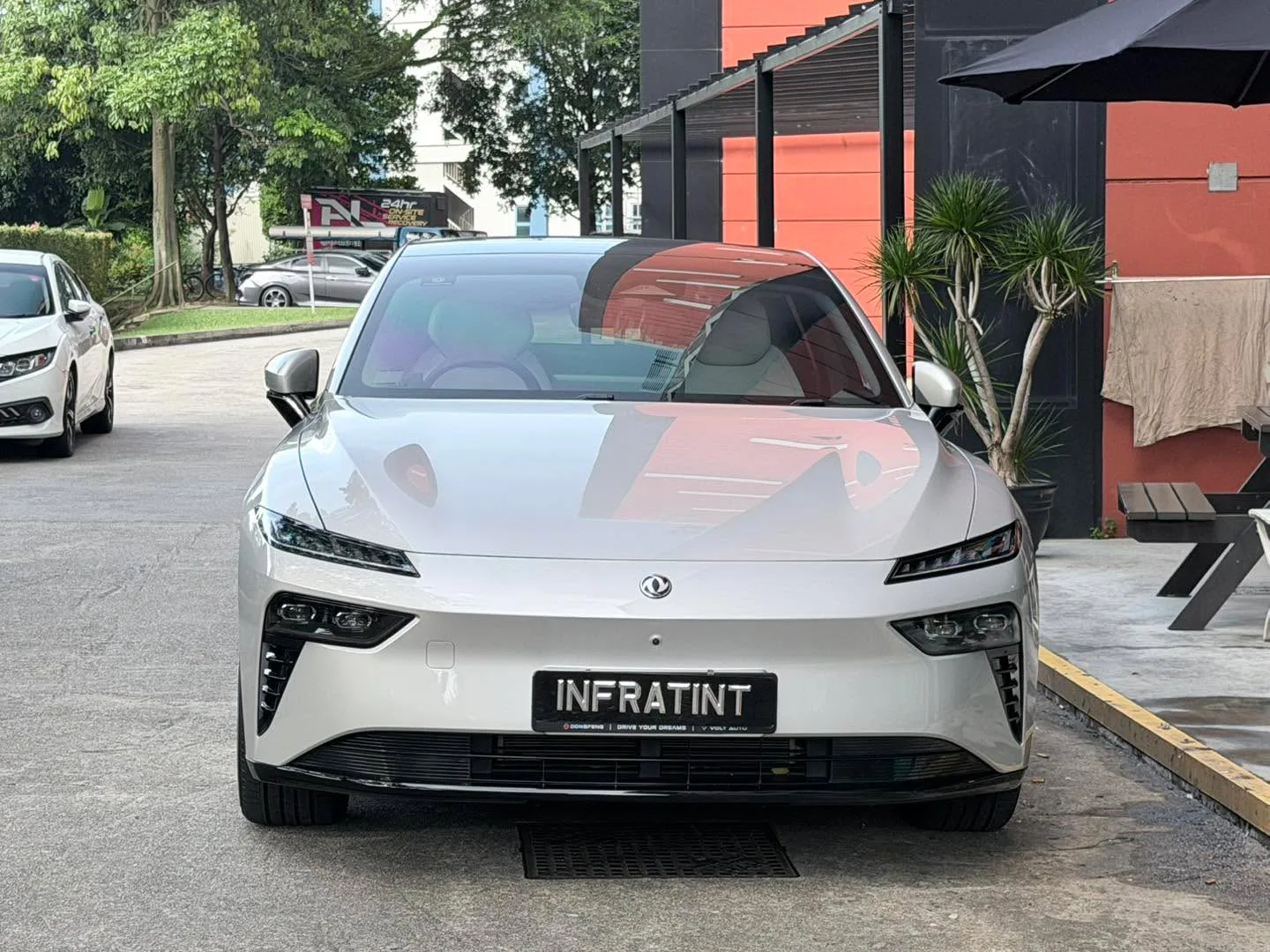 A white Dongfeng 007 sedan parked outside at the workshop entrance with tinted rear windows.