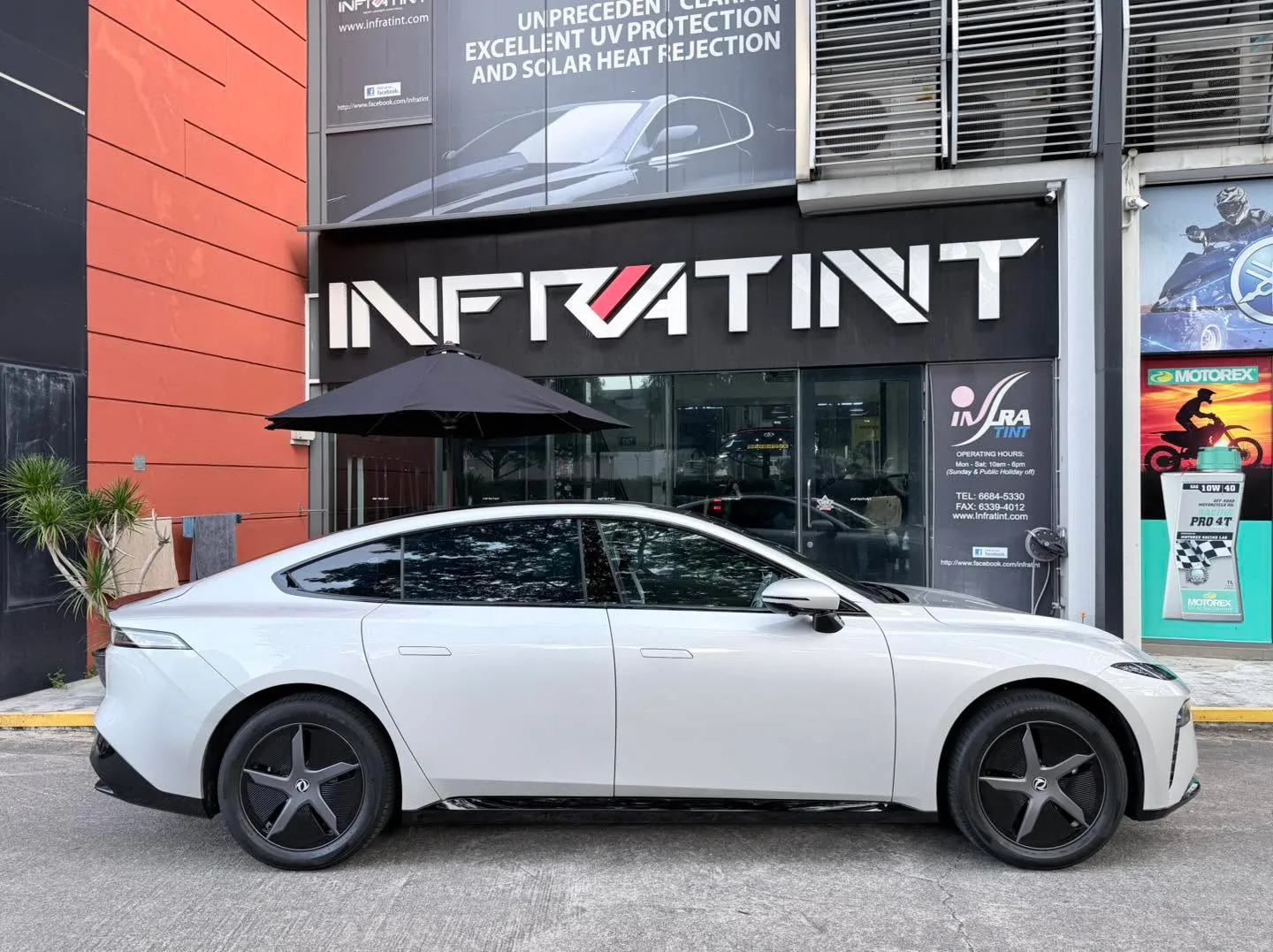 A white Dongfeng 007 sedan parked outside the Infratint storefront, showing the car's side profile with newly tinted windows.