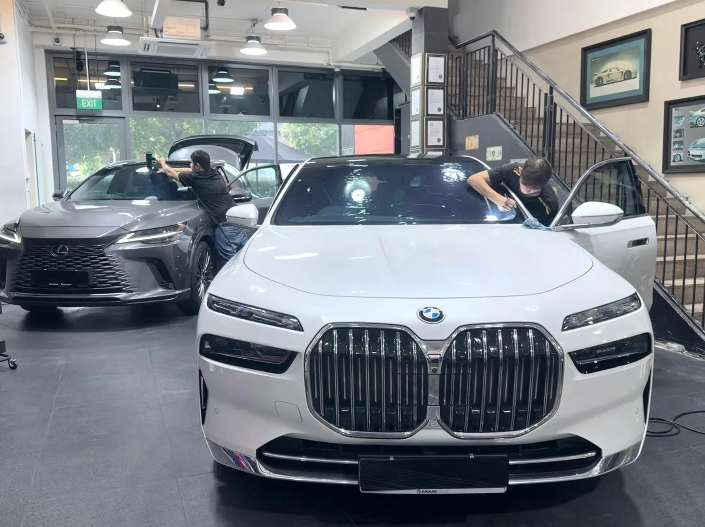 White BMW 7 Series with large kidney grille and grey Lexus RX SUV with door open during tinting.