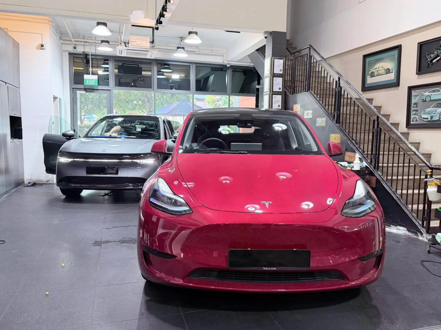 Red Tesla Model Y sedan with window tint being applied, blue-tinted glass on dark sedan behind.