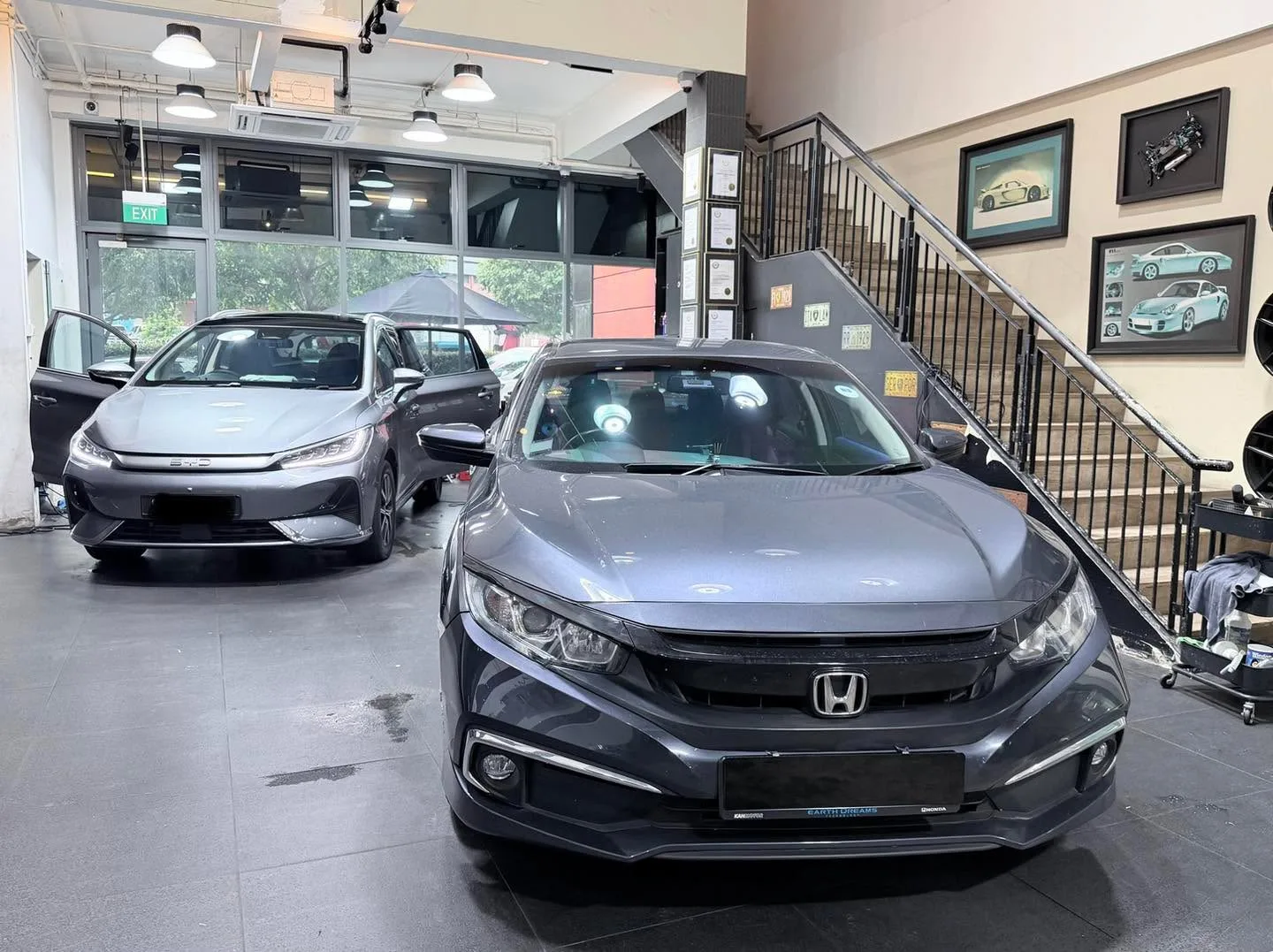 Grey Honda Civic sedan with door open for tinting, silver car beside it.