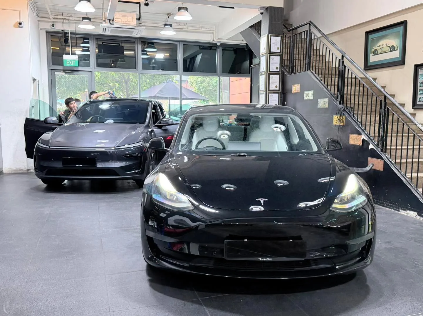 A white Tesla and a black Tesla parked indoors at the workshop.