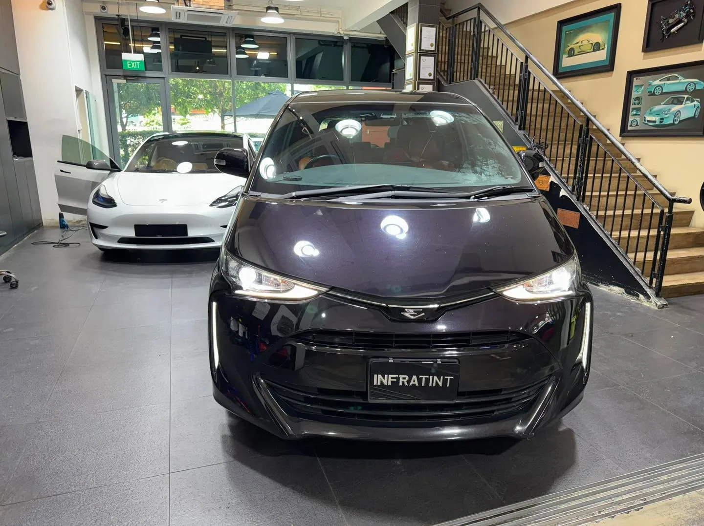 A black Tesla sedan with bright headlights parked indoors.