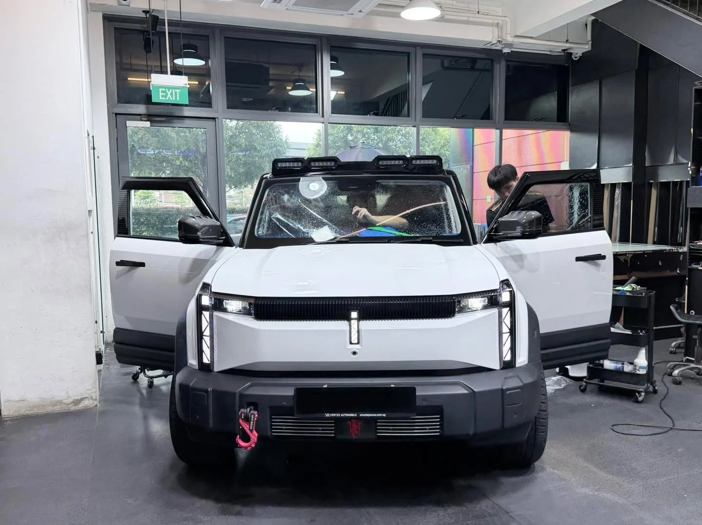 A white Rivian R1T with roof rack, undergoing window tint application.