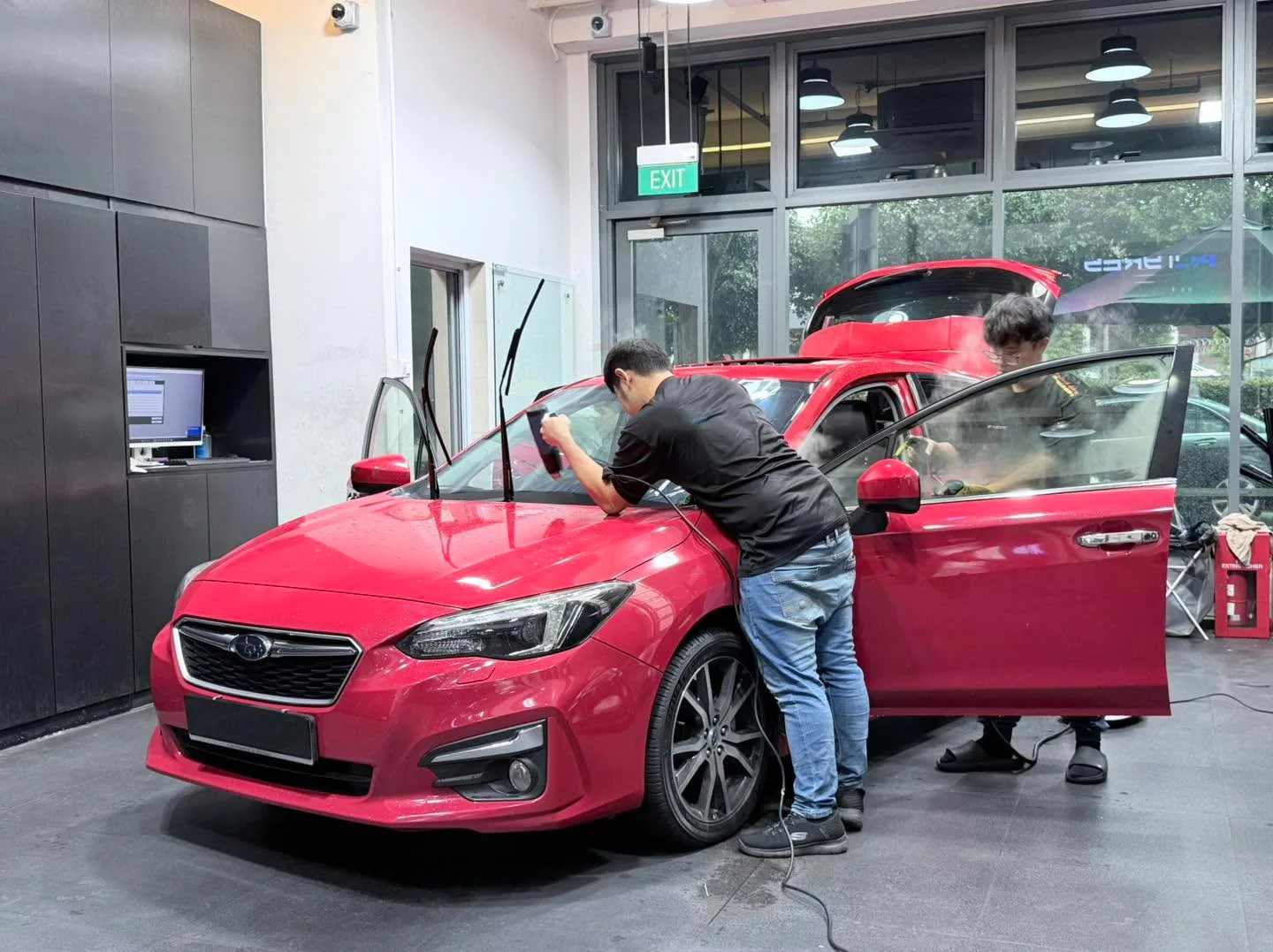 A bright red Subaru Impreza with technician applying window tint to the door.