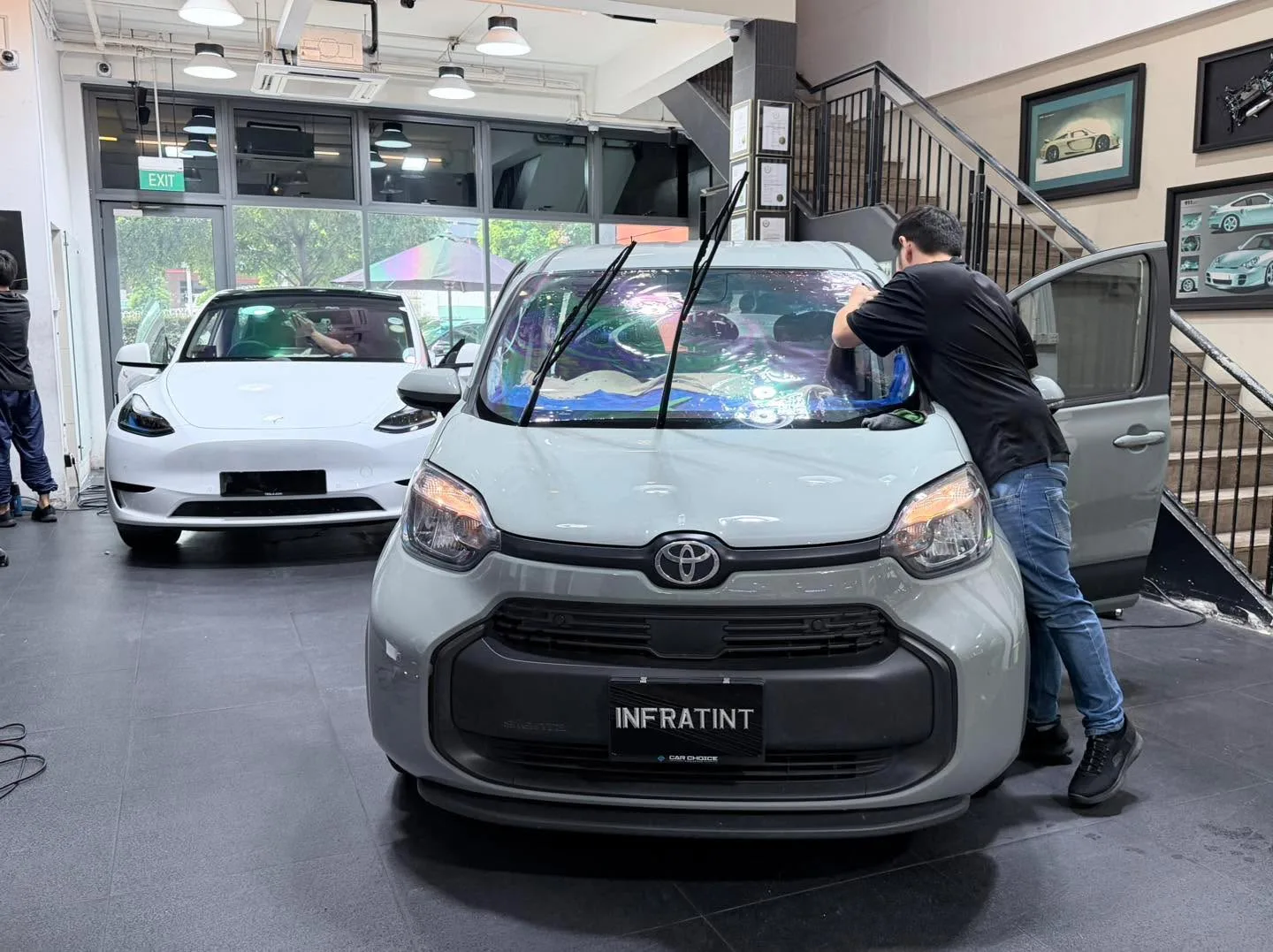 A white Toyota compact car with doors open in the workshop with a white Tesla visible behind.