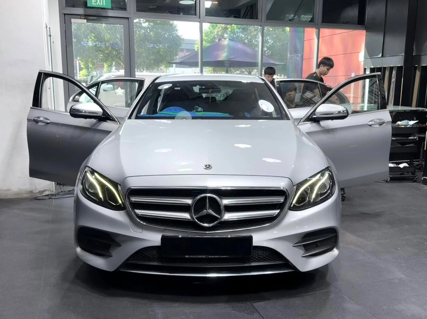 A white Mercedes-Benz sedan with doors open facing the camera in the workshop.