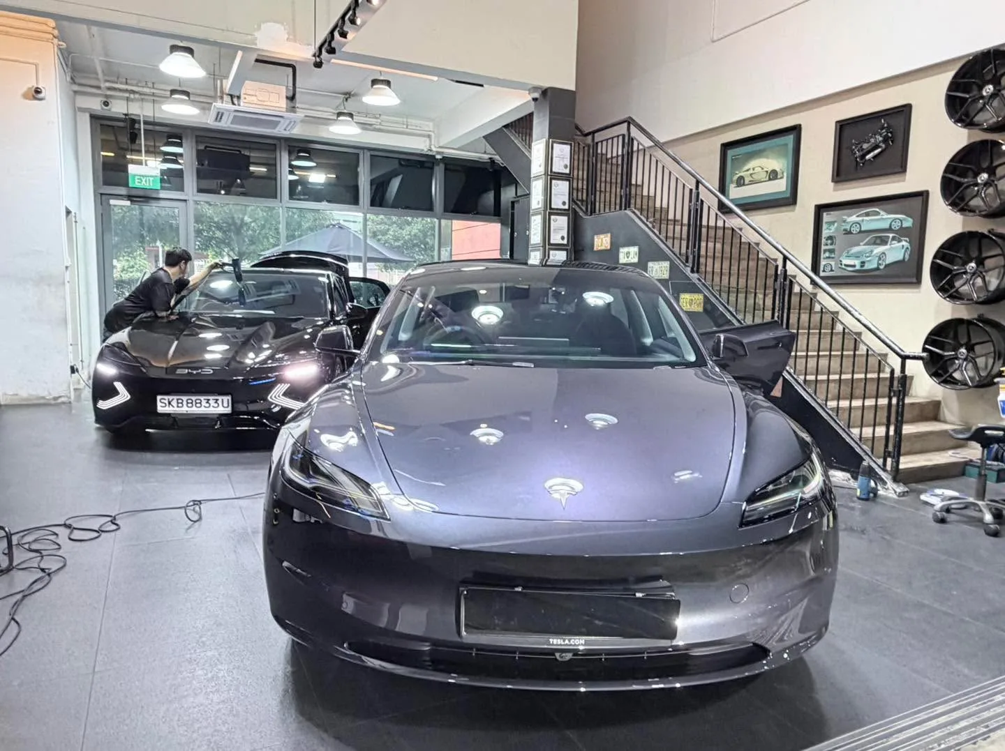 A white Tesla sedan with doors open in the workshop with another white vehicle behind.