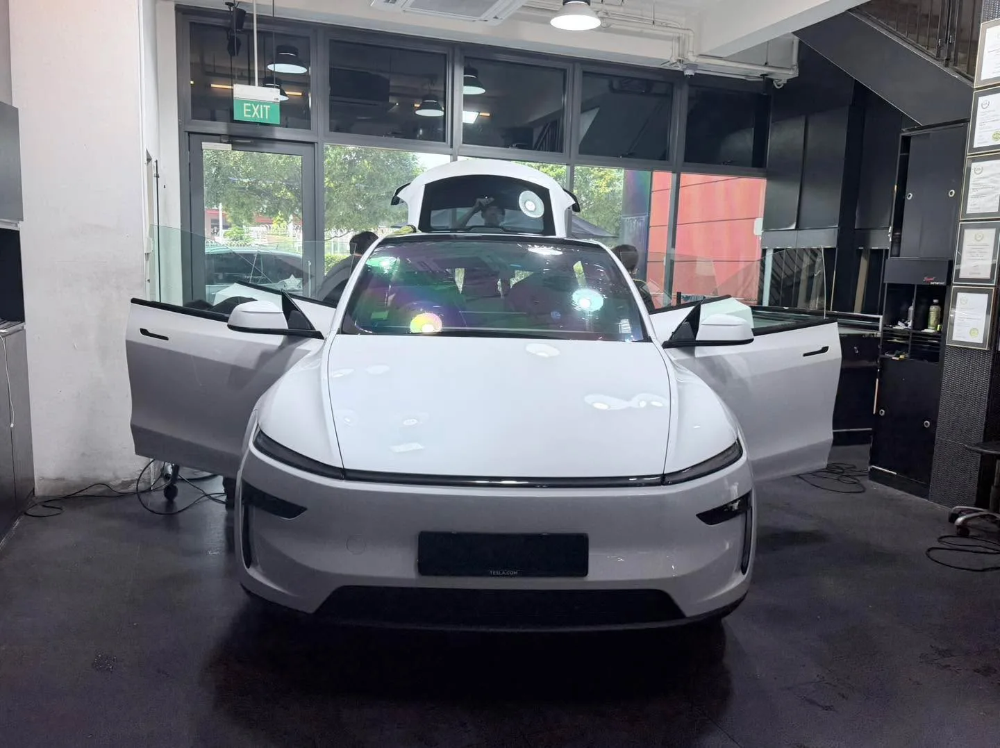 A white Tesla sedan facing forward with doors open in the workshop.