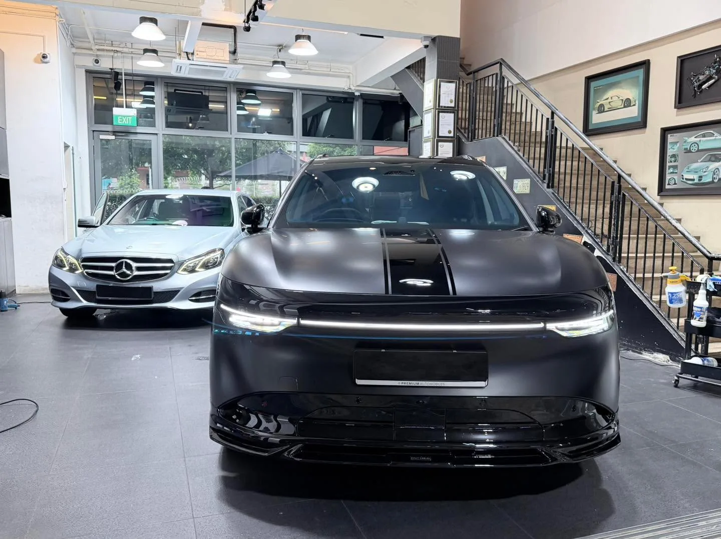 A black car with prominent kidney grille viewed from the front in a workshop.